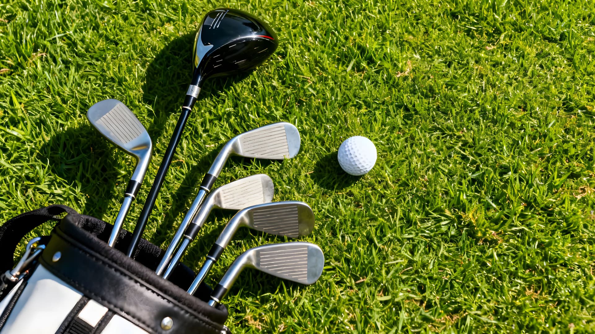 A set of golf clubs and a golf ball laying on bright green grass.