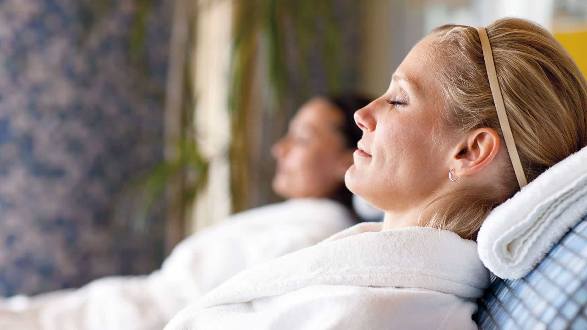 Two guests relaxing in premium white bathrobes at the Holland America Greenhouse Spa, a Club Orange exclusive amenity available on select sailings.