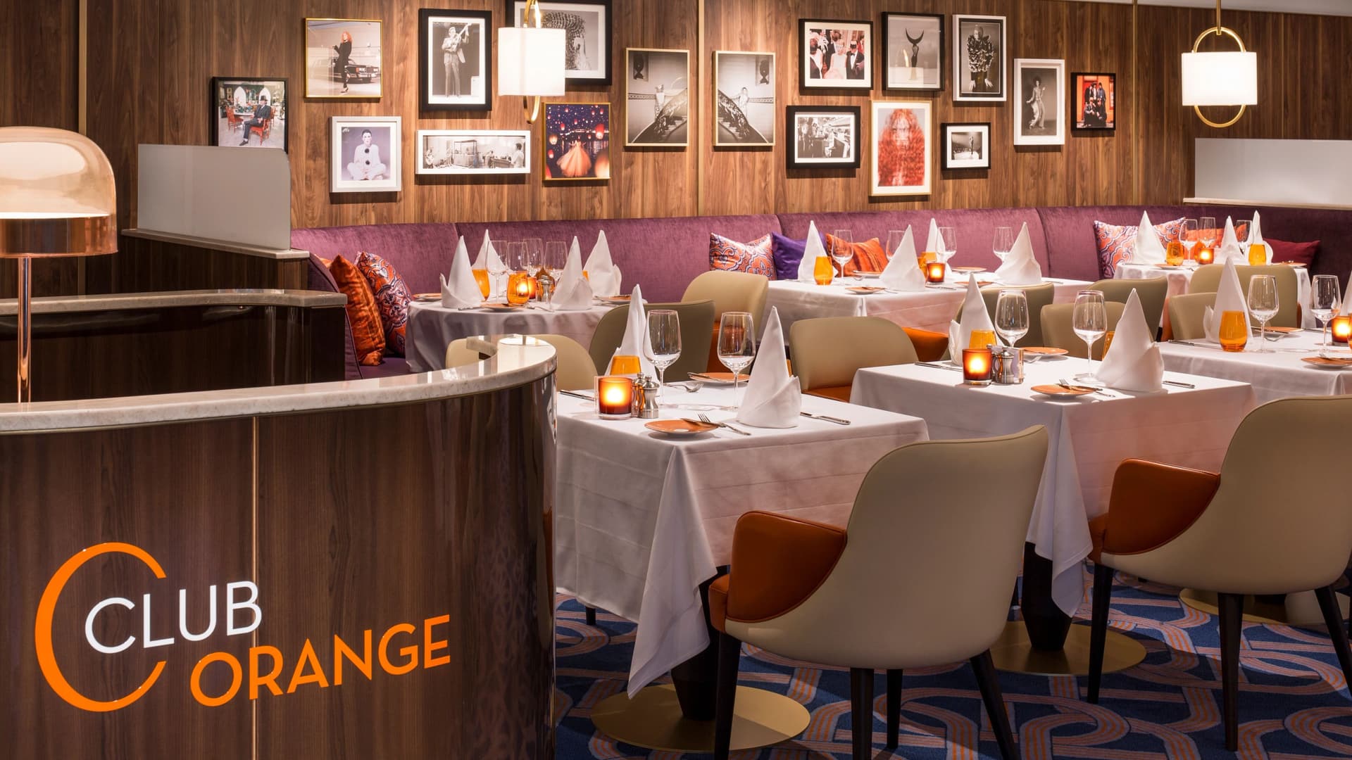 The elegantly set Club Orange private dining venue aboard a Holland America ship, featuring white linen tables, warm candlelight, and plush booth seating.