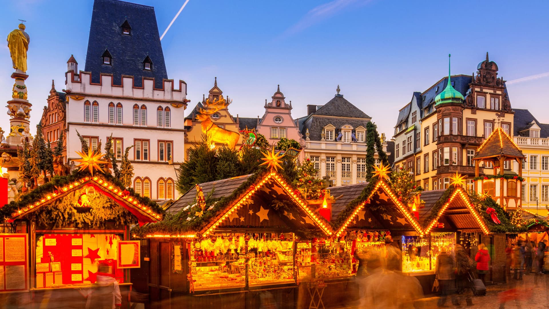 Christmas market booths lined up and lit by holiday lights with traditional european buildings behind.