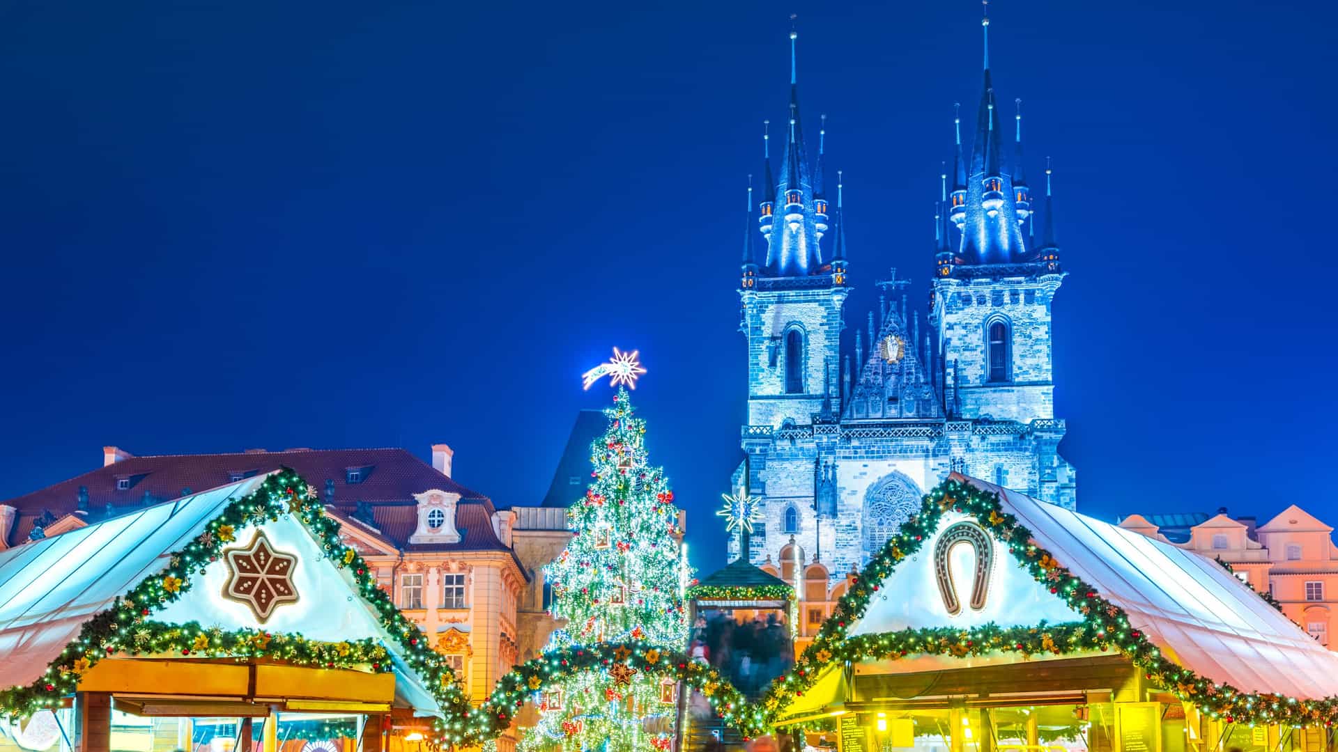 Two vendor booths and a large Christmas tree in front of a large cathedral in Prague during a Christmas market.