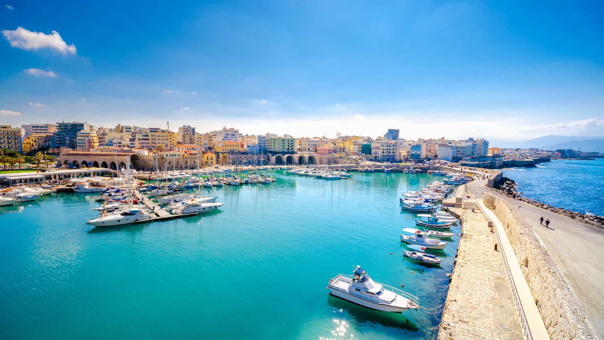 Holland America cruise ship docked at a vibrant Mediterranean port city, with yachts and colorful waterfront buildings under a clear blue sky.