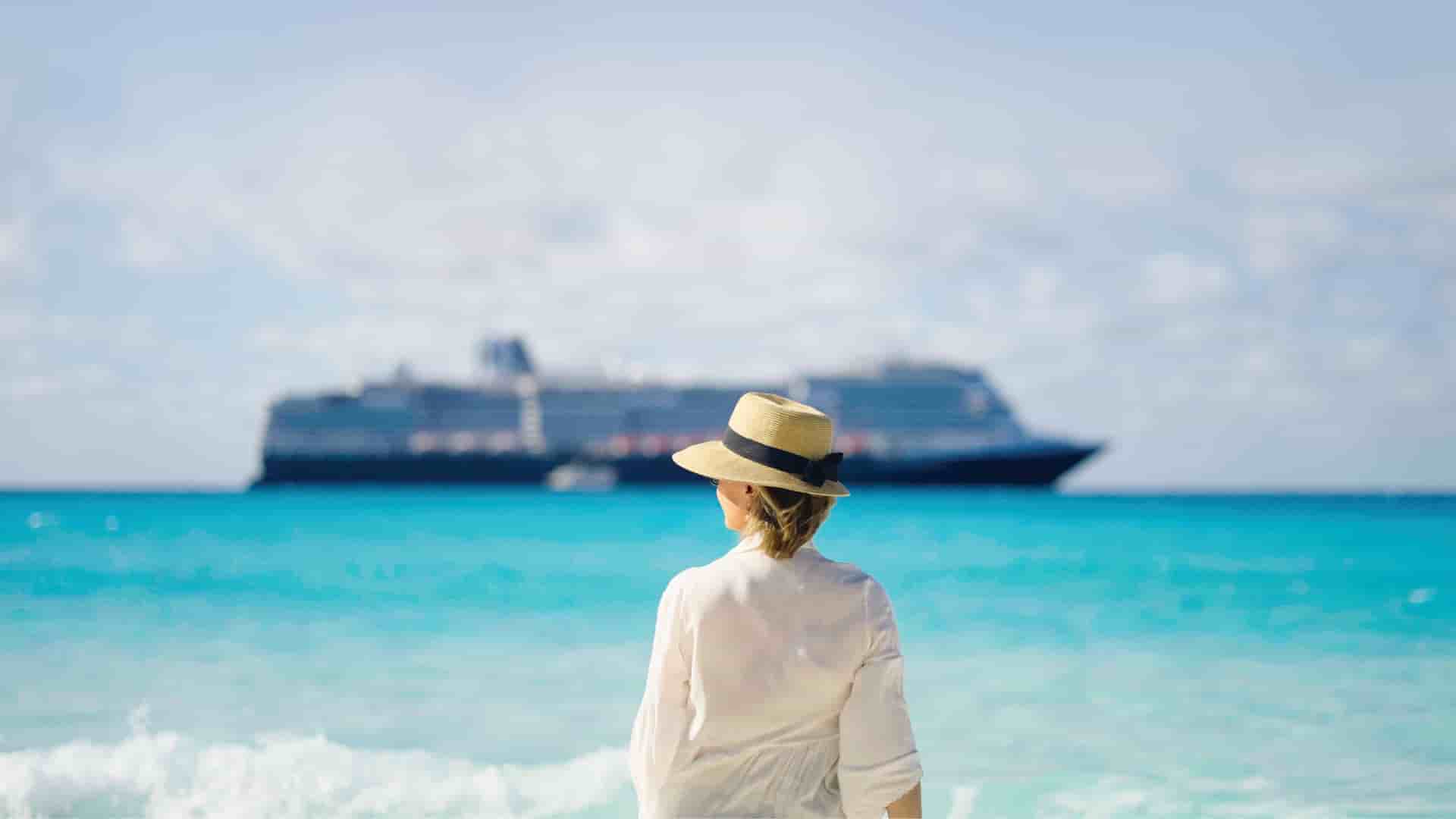 Woman standing on the beach of Half Moon Cay with a Holland America ship sailing in the background.