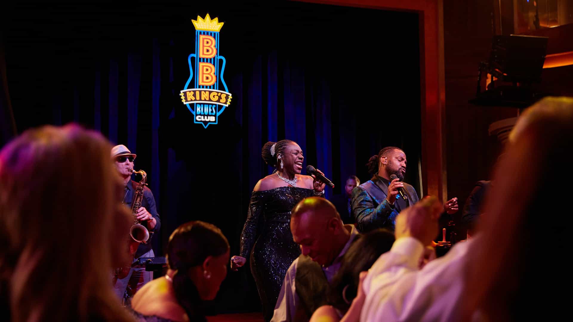 A soulful live music performance featuring vocalists and a saxophone player on stage at B.B. King's Blues Club onboard a Holland America ship.