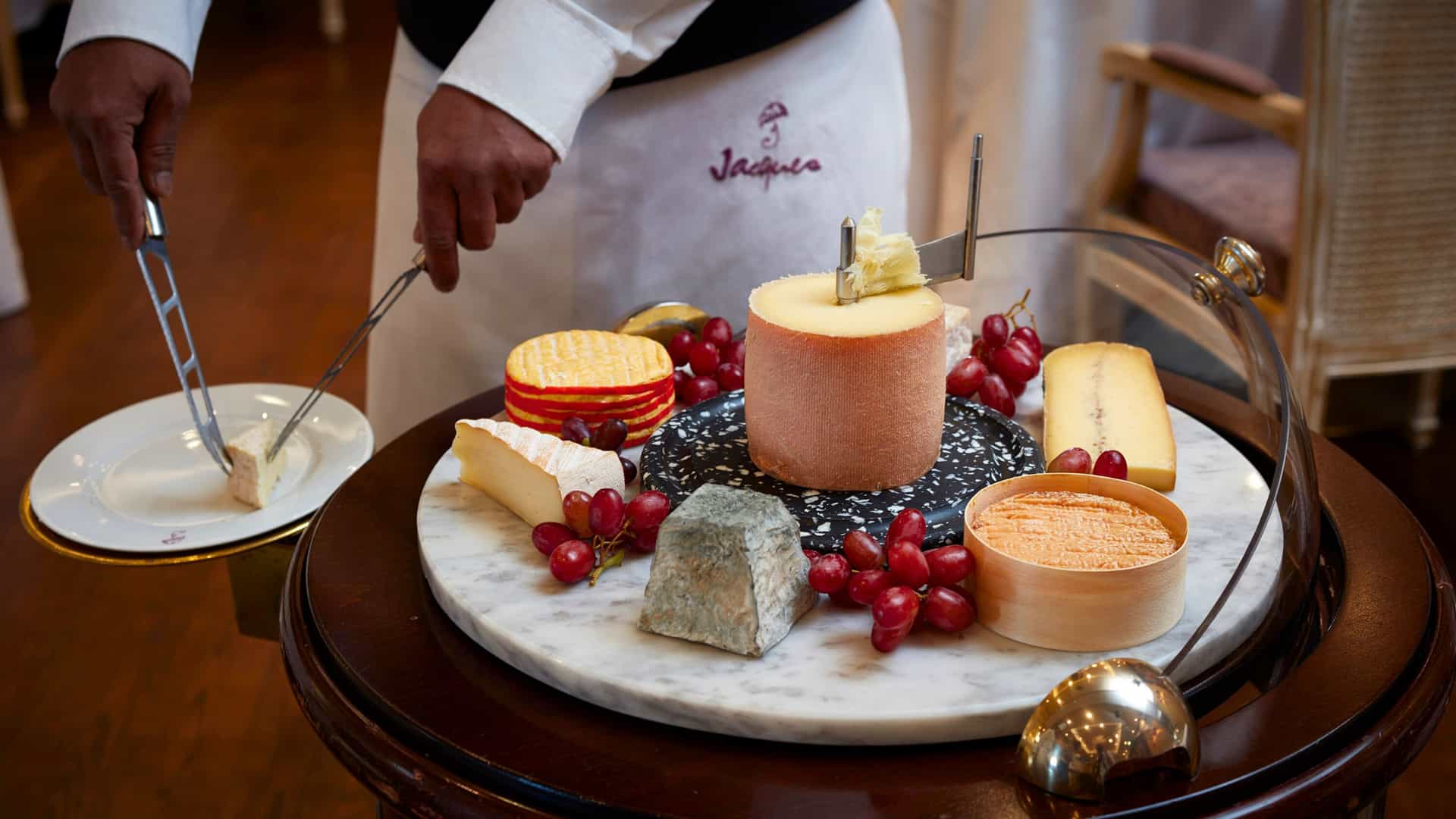 A waiter serving from a tray of fruits and artisan cheeses at Jacques & Jacques Bistro on an Oceania cruise.