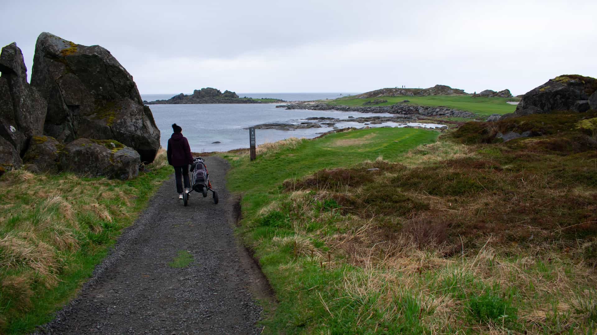 Golfer walking down a path with their clubs at the Lofoten Links golf course in Norway.