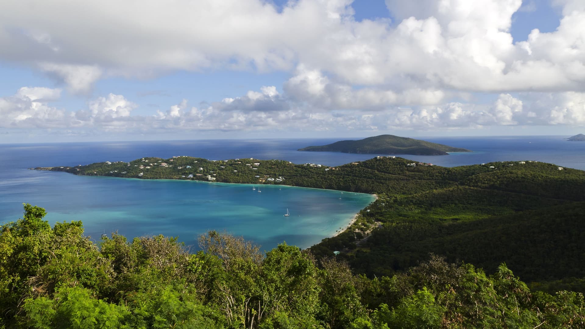Scenic view of Magen's Bay of St. Thomas from the top of Drake's Seat with lush green, blue waters, and white clouds.