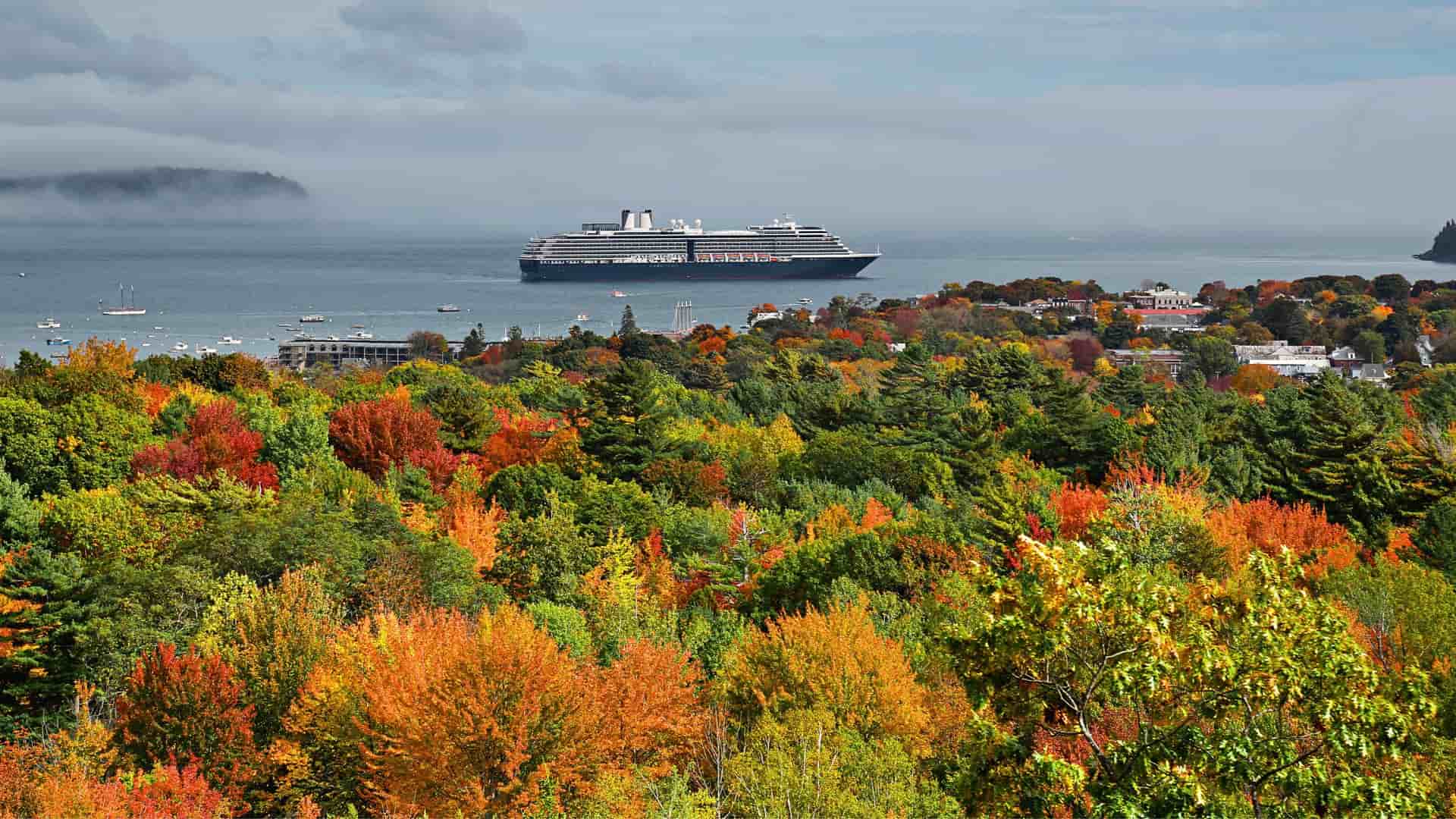 Bright orange fall foliage in Maine with a cruise ship sailing in the background.