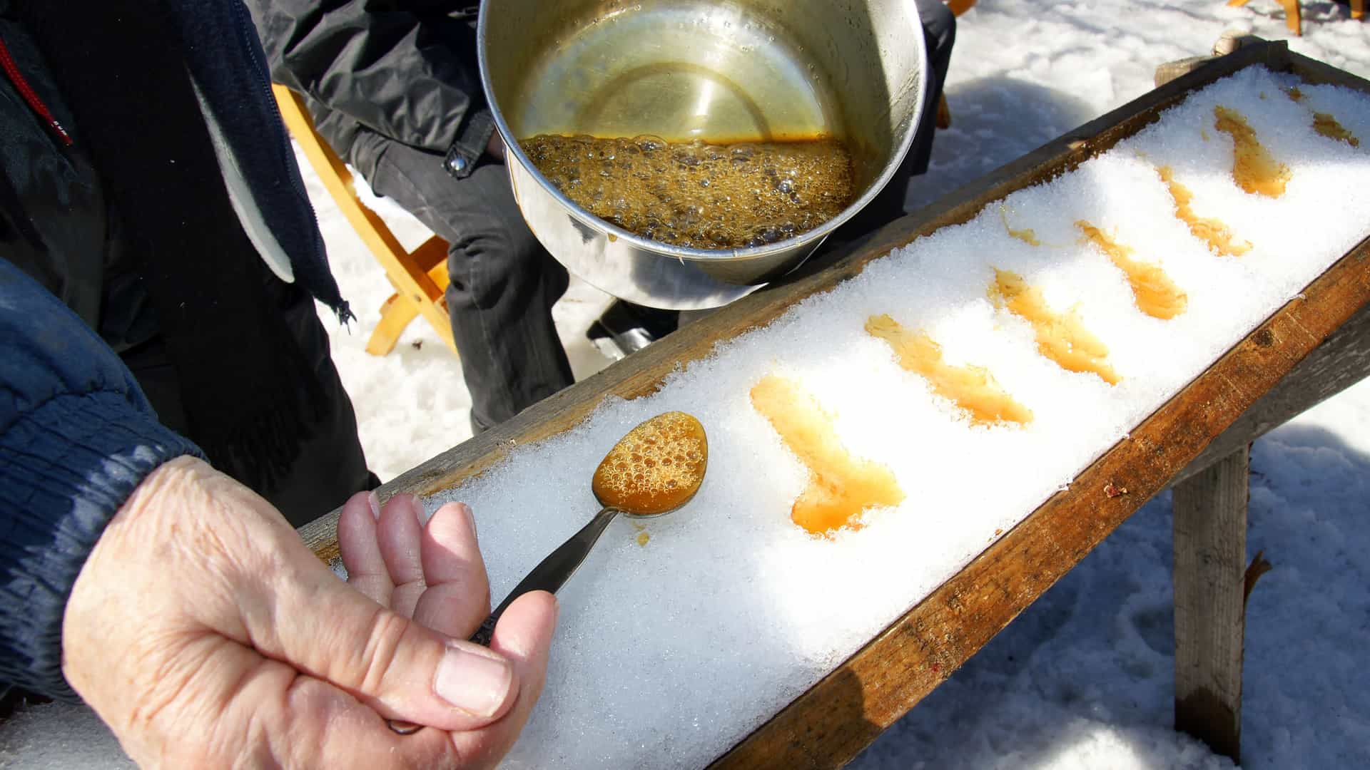 A close up shot of hot maple syrup being poured onto cold snow at a Canadian sugar shack in order to make taffy.