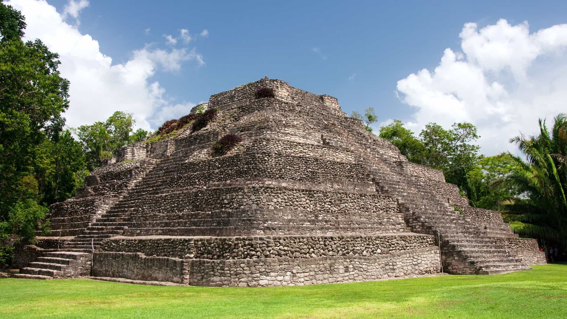 Ancient Mayan ruins in Mexico, showcasing stone structures and lush greenery under a clear blue sky.