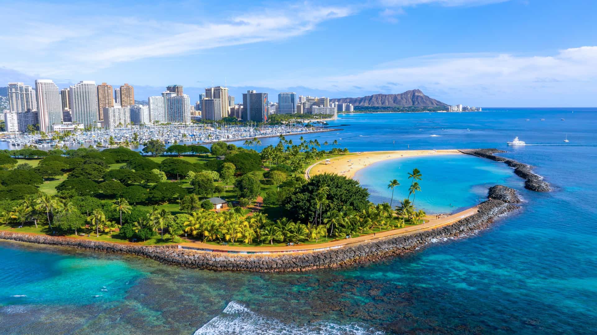 Coastal cityscape of Honolulu, Oahu, Hawaii, with clear blue water, coral reefs, and Diamond Head in the background.