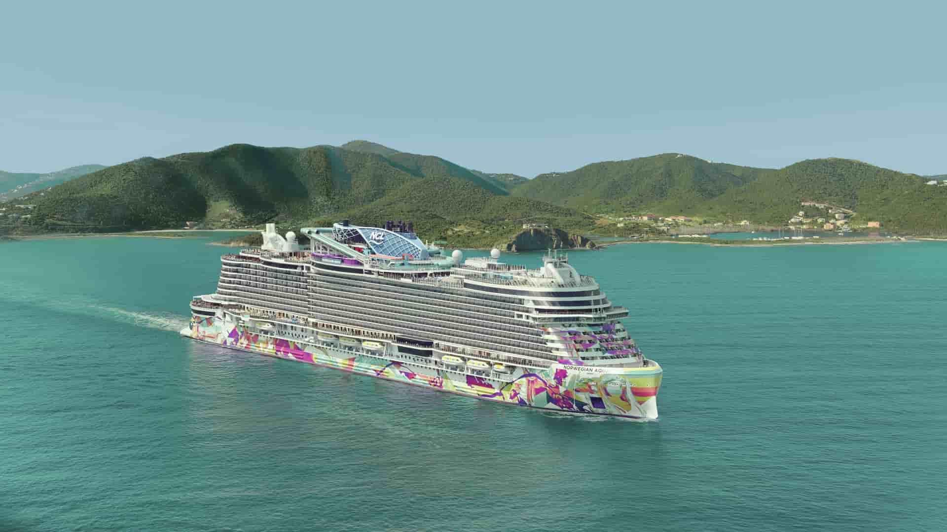 Aerial shot of Norwegian Aqua sailing through Tortola with grassy mountains in the background and a clear blue sky.