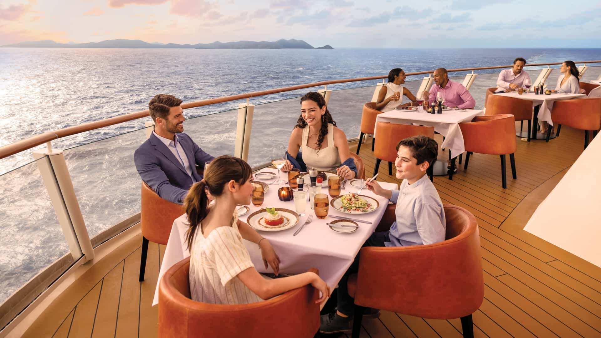 A family of four enjoying an outdoor waterfront dinner at sunset aboard Norwegian Encore, with ocean views and candlelit table settings at one of Norwegian Cruise Line's open-air dining venues.