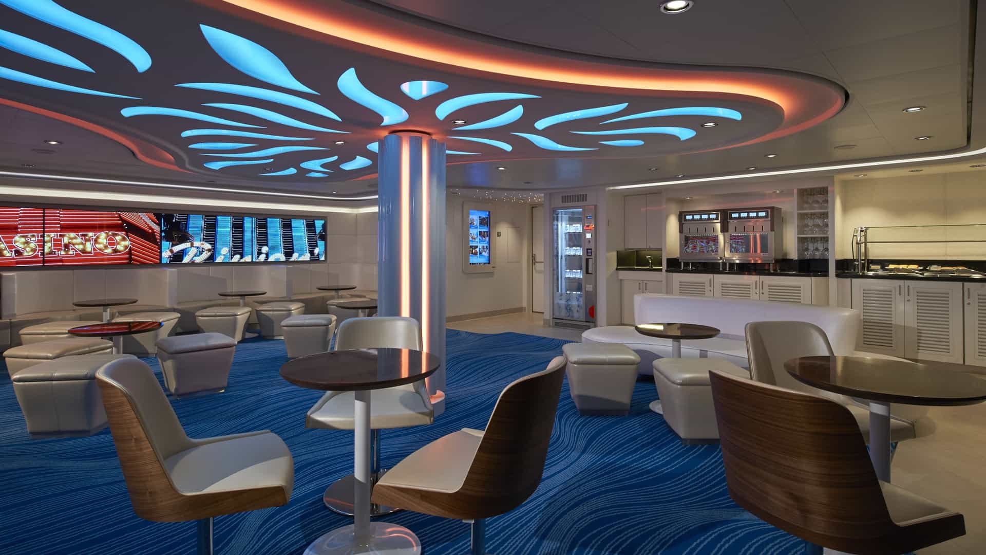 Studio Lounge on Norwegian Escape with round tables, cushioned stools, a serving counter and a lit ceiling design.