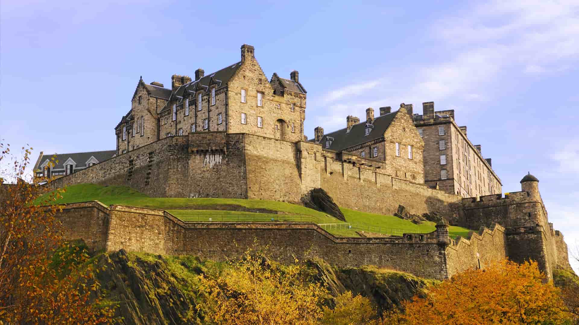 Edinburgh Castle perched on a hill, surrounded by vibrant autumn foliage and a clear blue sky.