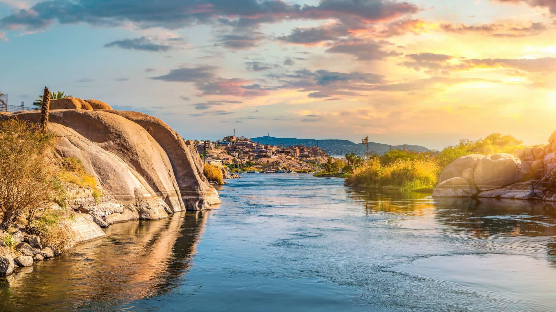 Norwegian Cruise Line guests enjoying a sunset felucca ride on the Nile River in Aswan, Egypt, with ancient temples or landscapes in the background.