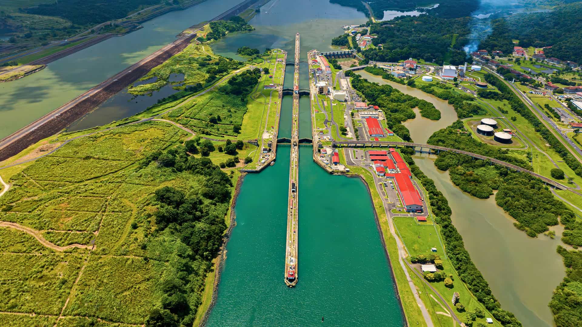 Aerial view of a Norwegian Cruise Line ship transiting the Miraflores Locks of the Panama Canal in Central America, showcasing the engineering marvel and lush surroundings.