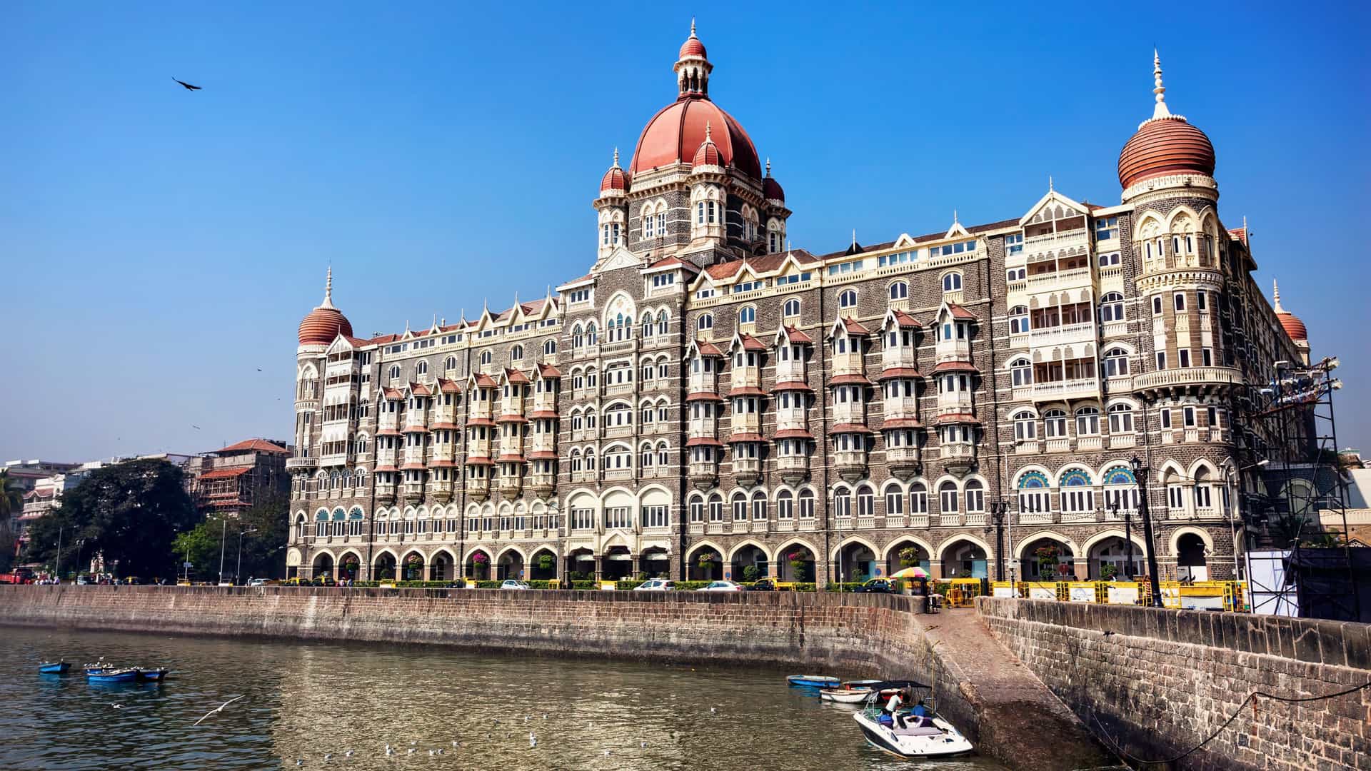 The iconic Taj Mahal Palace Hotel in Mumbai, India, viewed from the waterfront with a boat in the foreground, a popular port for Oceania cruises.
