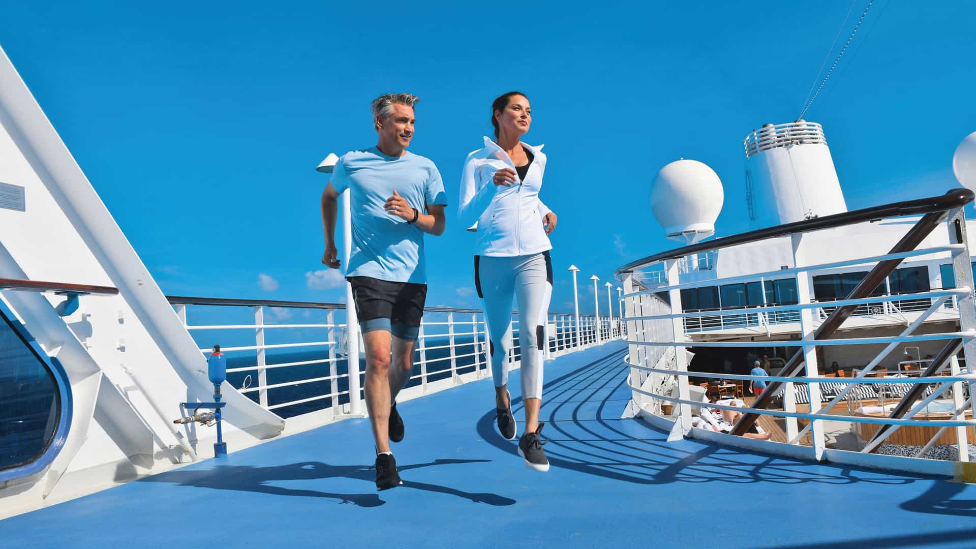 A couple dressed in athletic gear, running along the track aboard an Oceania ship.