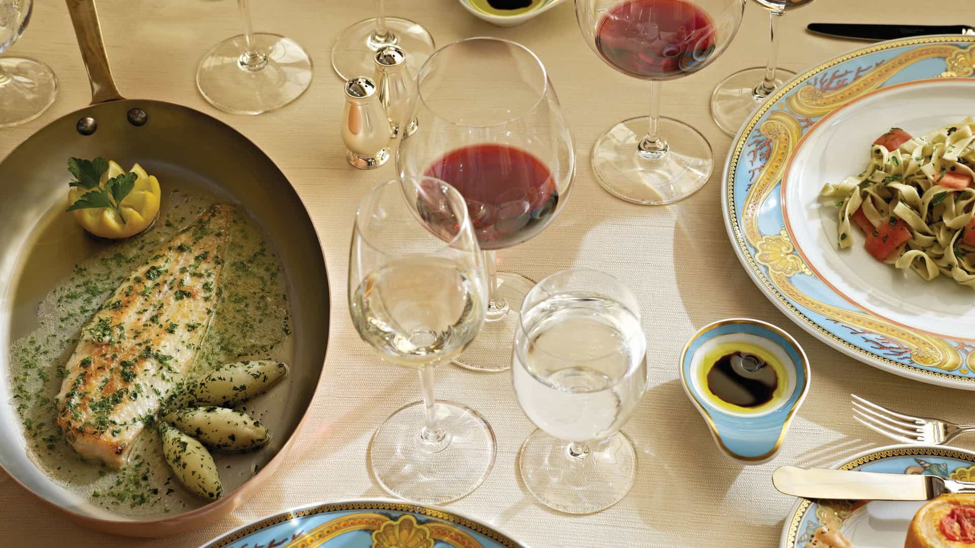 Pan-seared branzino with herb butter and potato gnocchi served tableside in a copper pan alongside fettuccine on custom Versace china at Toscana on Oceania Cruises.