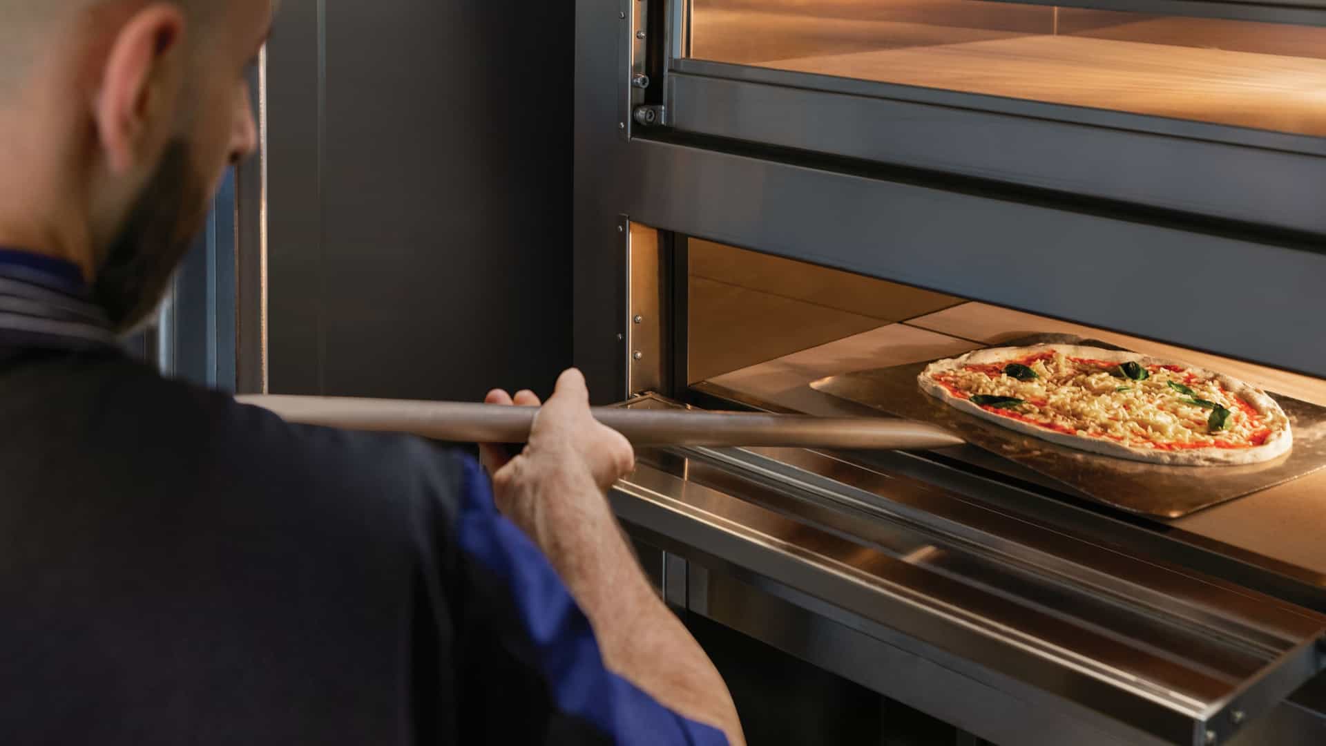 A chef sliding a freshly made margherita pizza into a stone deck oven at the Waves Grill pizzeria on Oceania Cruises.