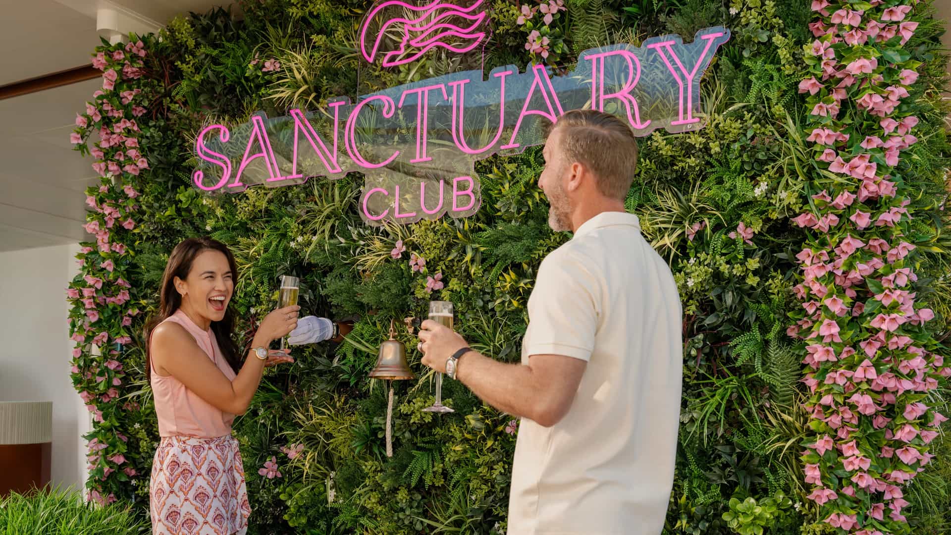 Couple celebrating with champagne at the Sanctuary Club floral wall on Sun Princess.