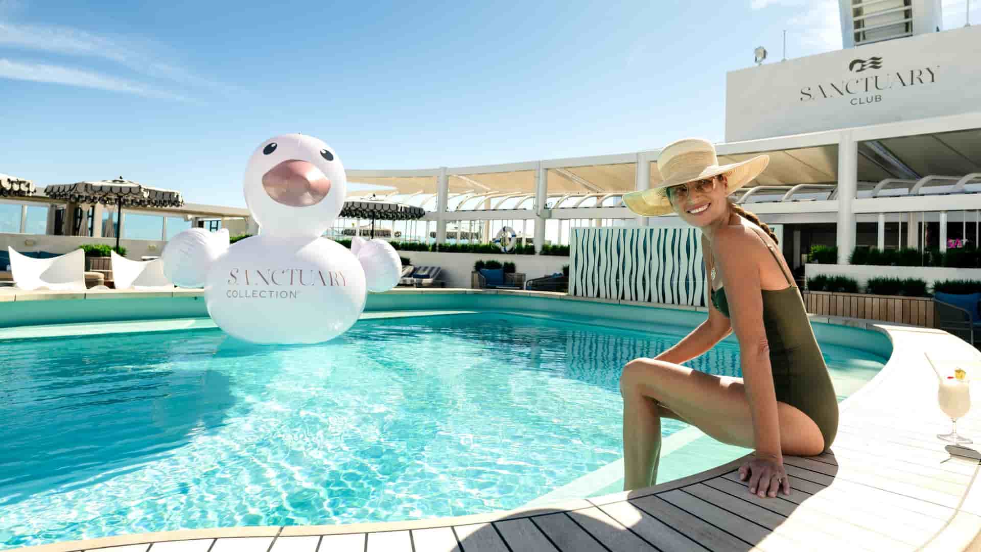 Woman relaxing poolside at the Sanctuary Club on Sun Princess, with a large inflatable Sanctuary Collection duck float in the turquoise pool.