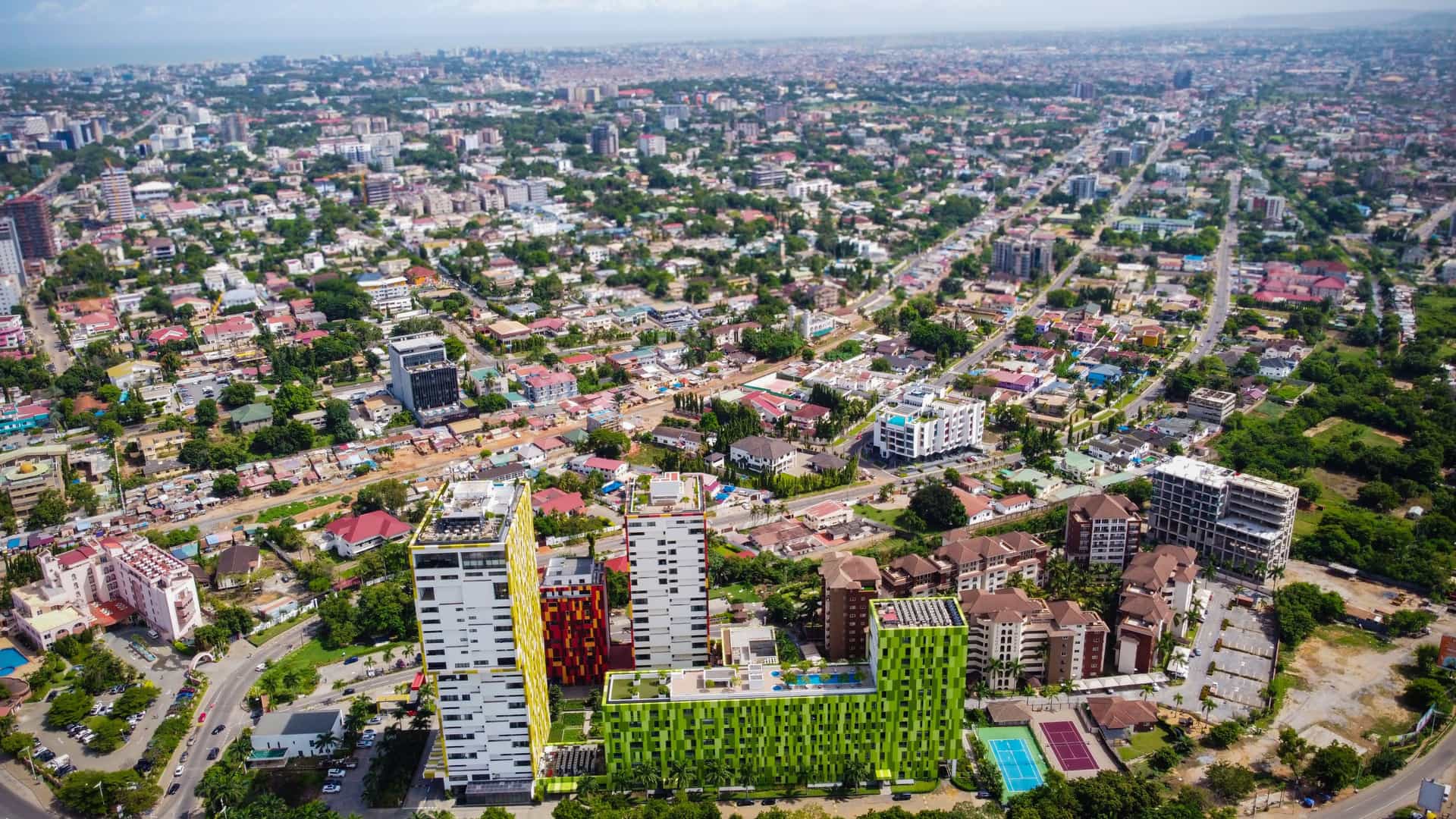 An aerial view of Accra, Ghana, showcasing a dense, sprawling cityscape with a mix of modern high-rise buildings and residential areas.