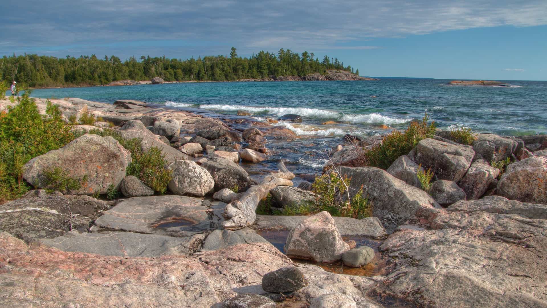 A beautiful rocky shoreline of Lake Superior in Algoma, Canada, with a small stream flowing between large boulders into the turquoise water.