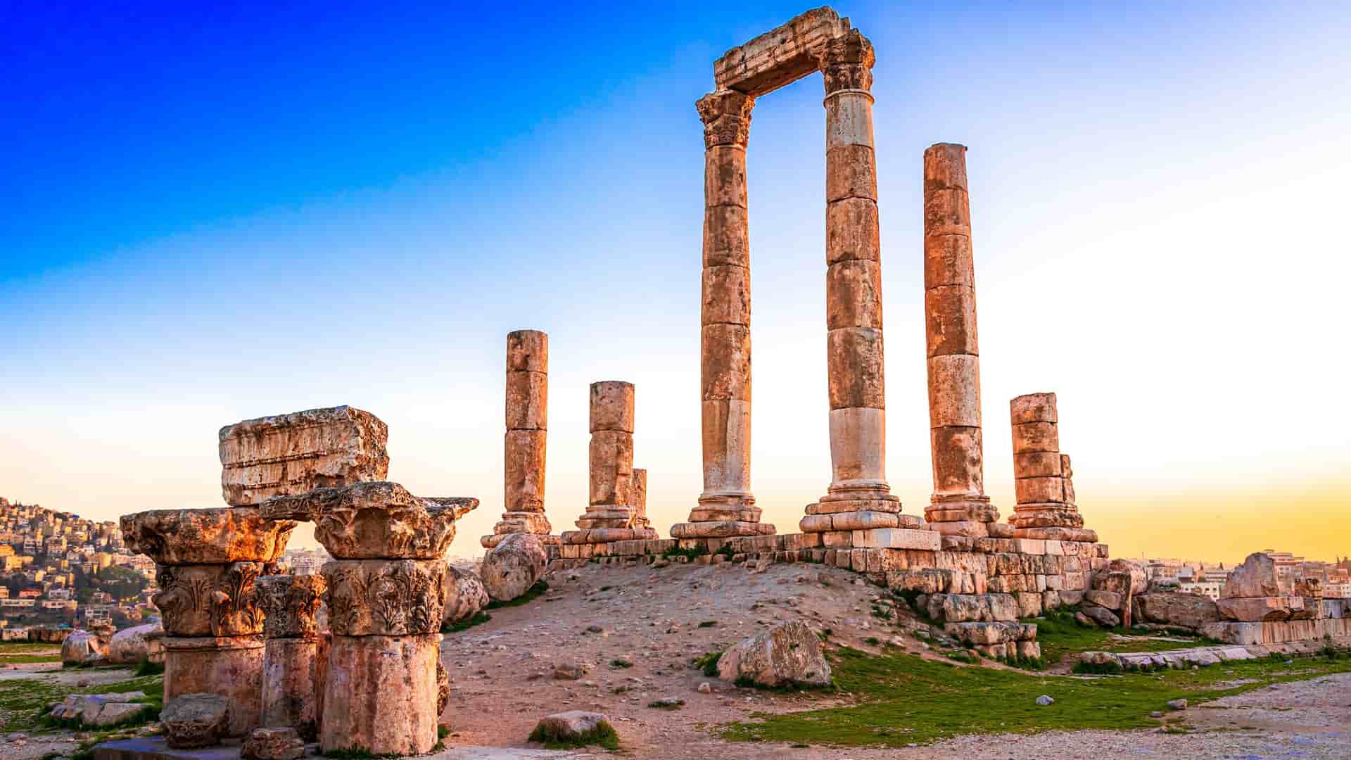 A breathtaking sunset shot of the ancient ruins of the Temple of Hercules, with its massive columns silhouetted against a golden-orange sky on the Citadel Hill in Amman, Jordan.