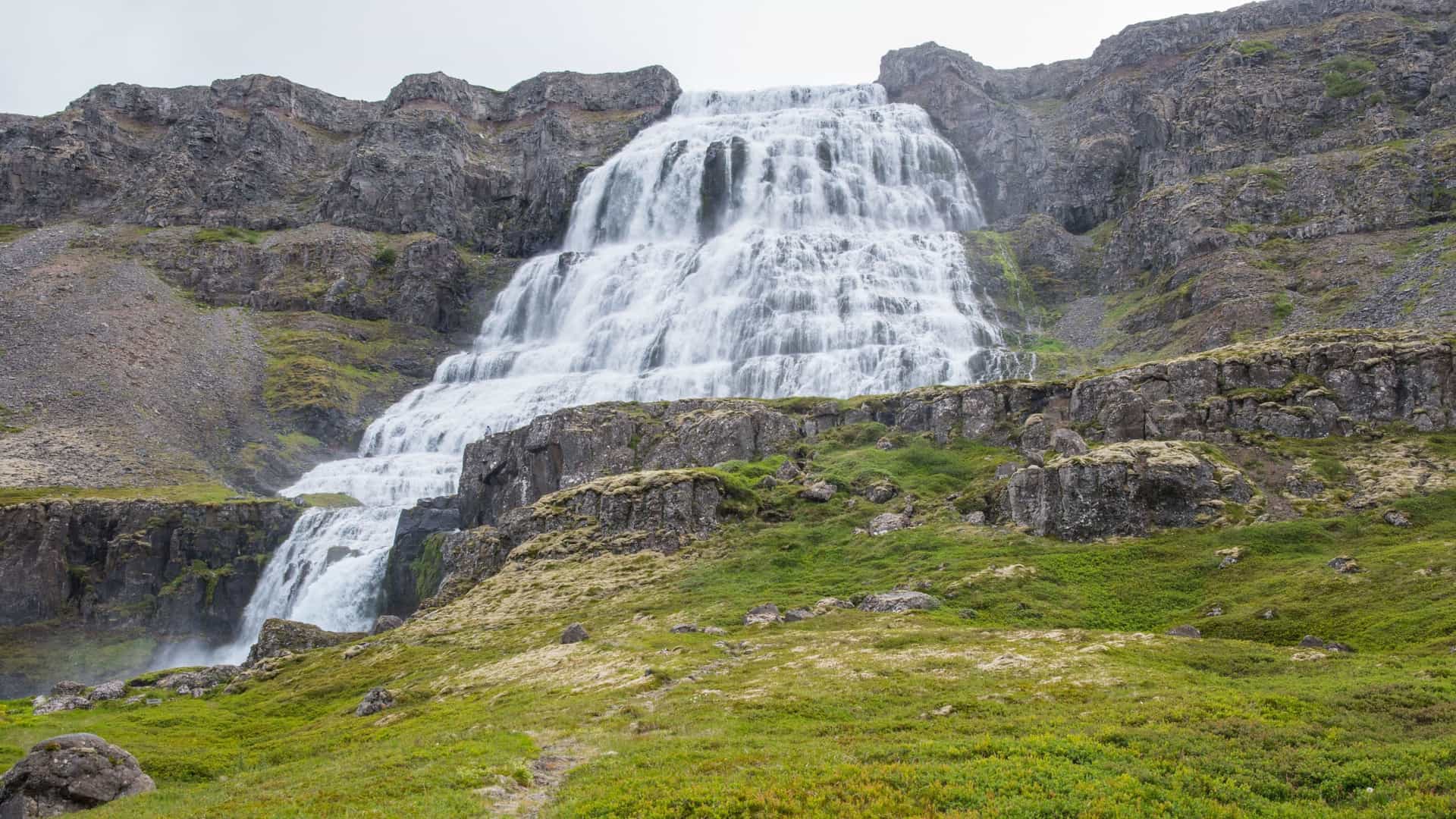 A stunning view of the powerful Dynjandi waterfall cascading over multiple tiers of dark rock and green moss in the Arnarfjörður fjord in Iceland.