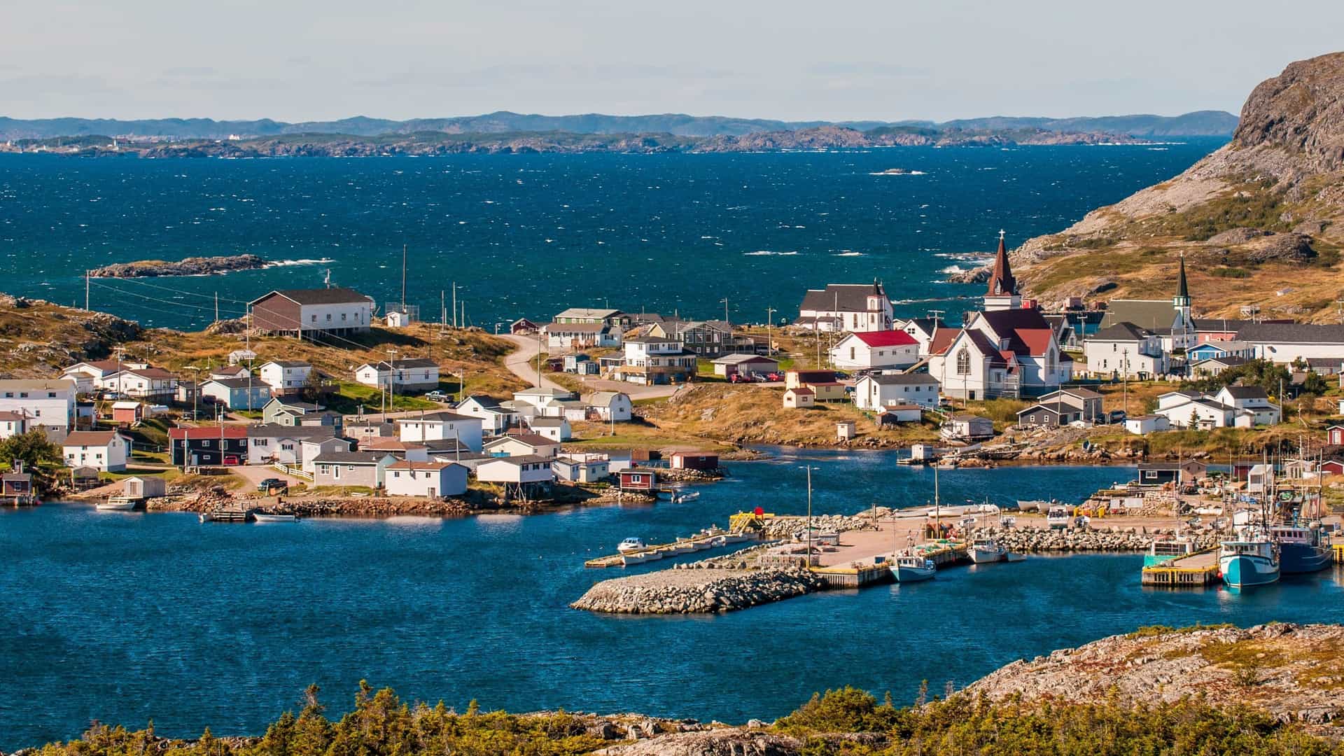 A coastal village with colorful houses and a prominent church steeple, nestled on a rocky bay with fishing boats moored at a pier on the rocky Battle Island.