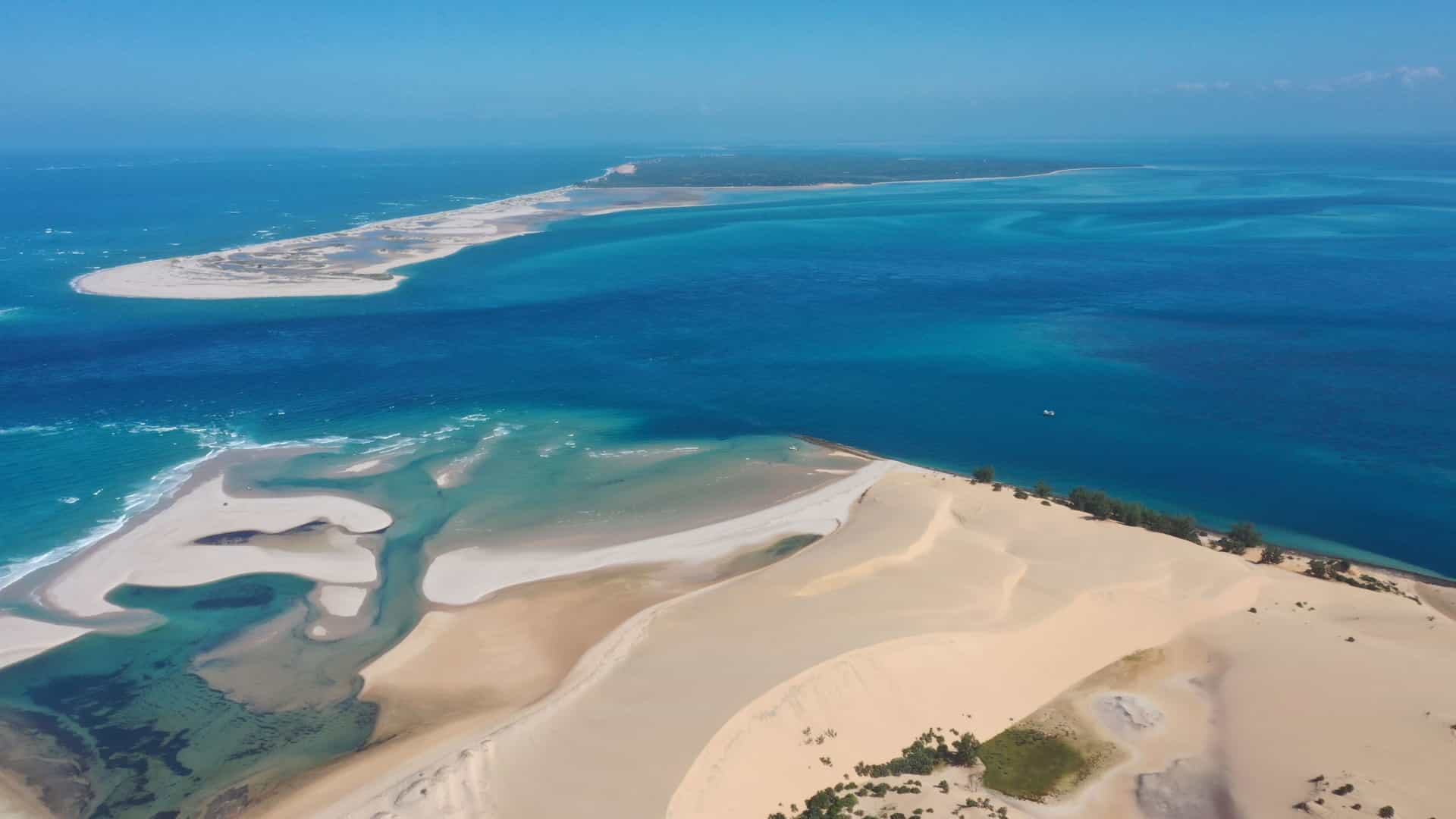 An aerial view of Bazaruto Island, showcasing expansive white sand dunes, pristine turquoise waters, and lush green vegetation under a clear sky.