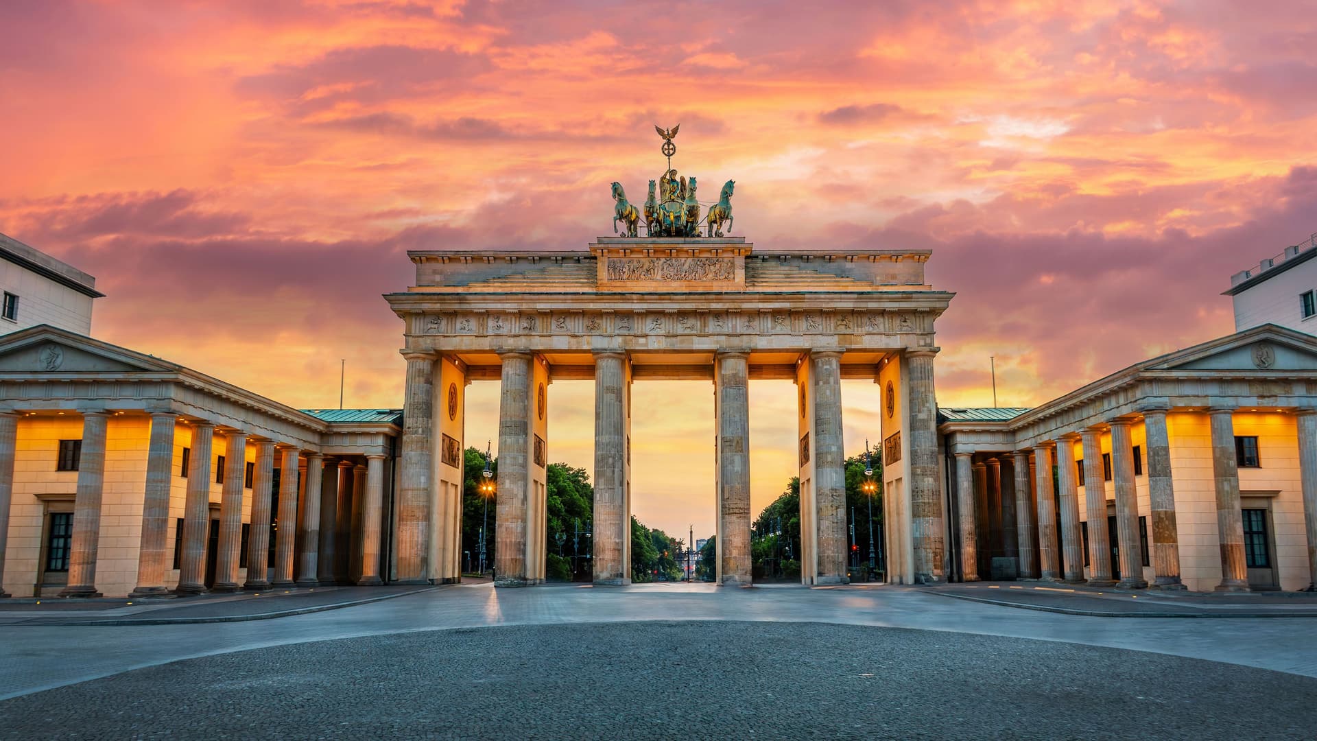 The famous Brandenburg Gate in Berlin, Germany, at sunrise, with a stunning orange and pink sky.