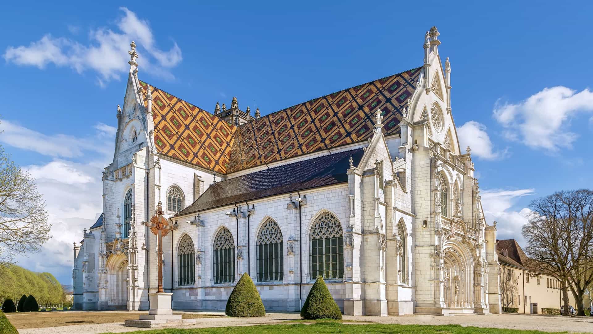 A magnificent view of the Royal Monastery of Brou in Bourg-en-Bresse, France, showcasing the ornate Gothic architecture and its iconic patterned tile roof.