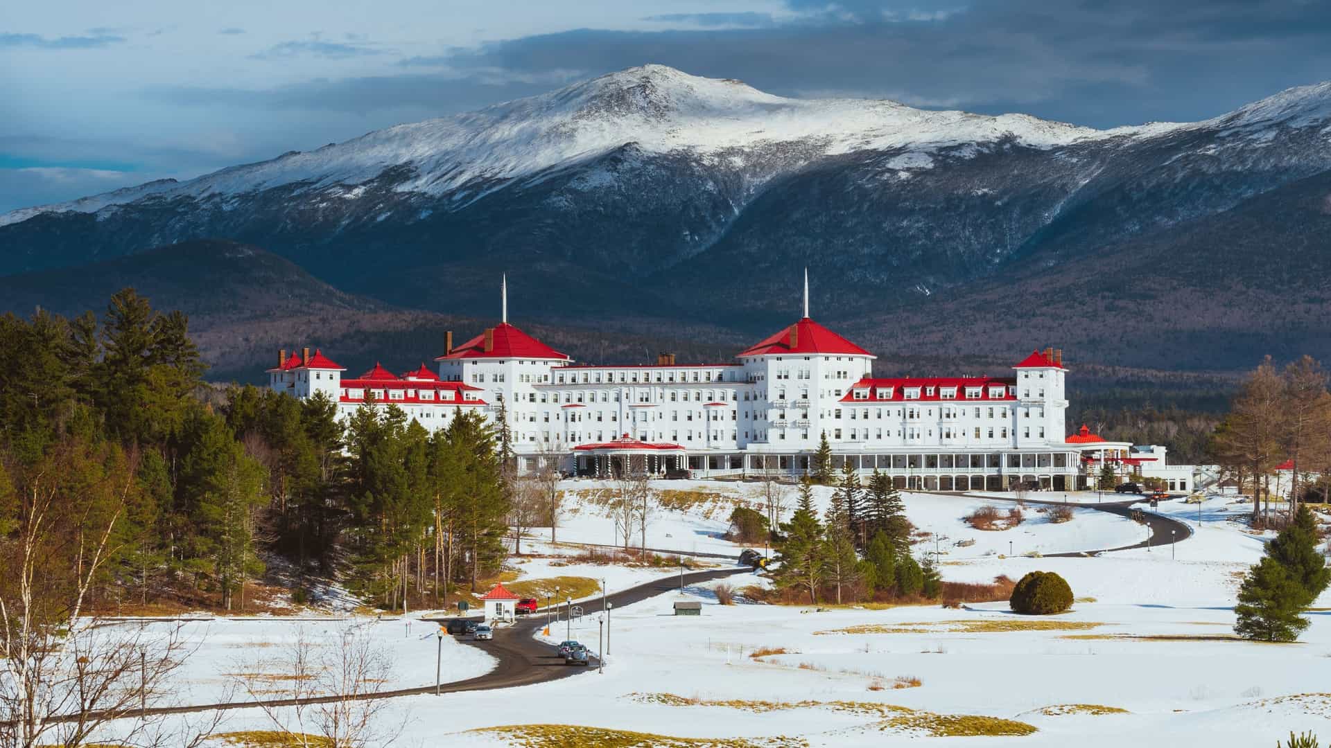 The grand, white Omni Mount Washington Hotel with its red roof stands against the snow-covered Presidential Range in Bretton Woods, New Hampshire.