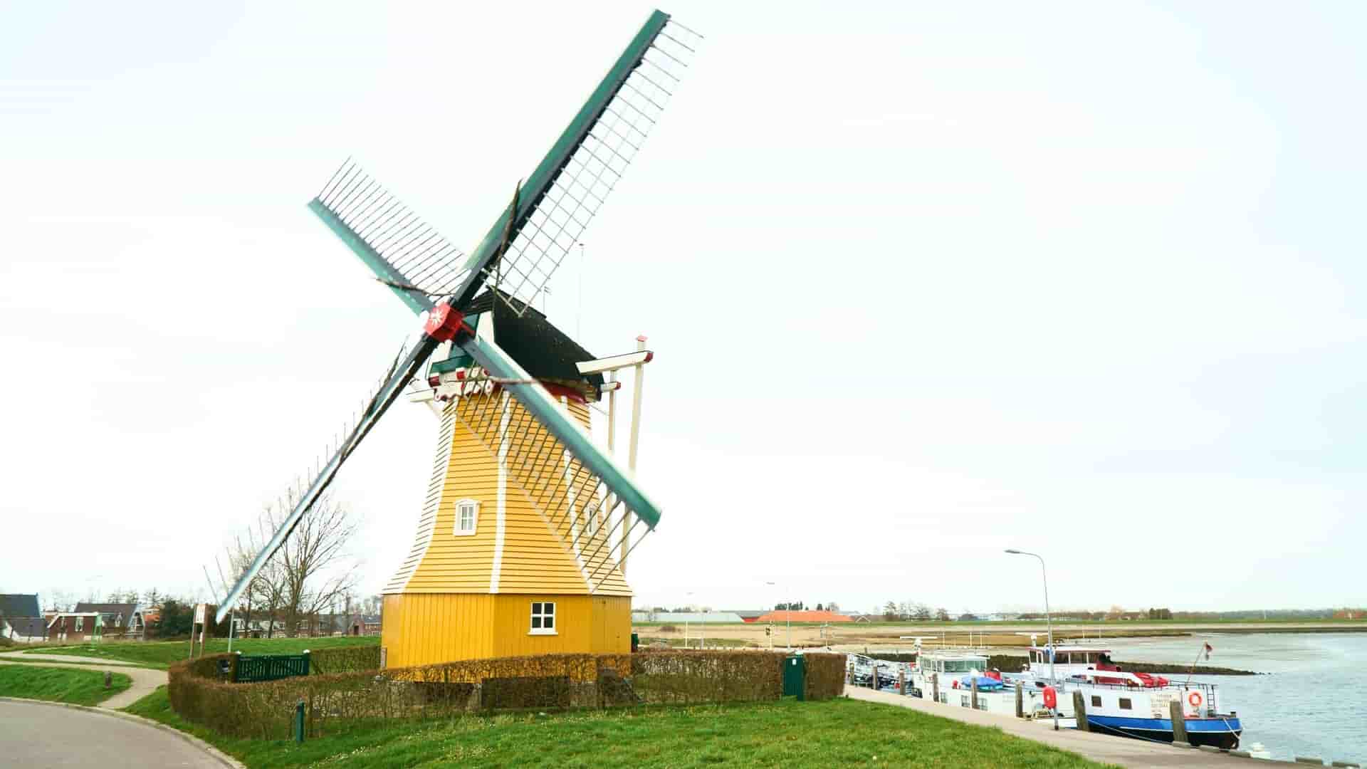 A classic yellow windmill, a famous landmark of Bruinisse, Netherlands, stands next to a small harbor with boats.