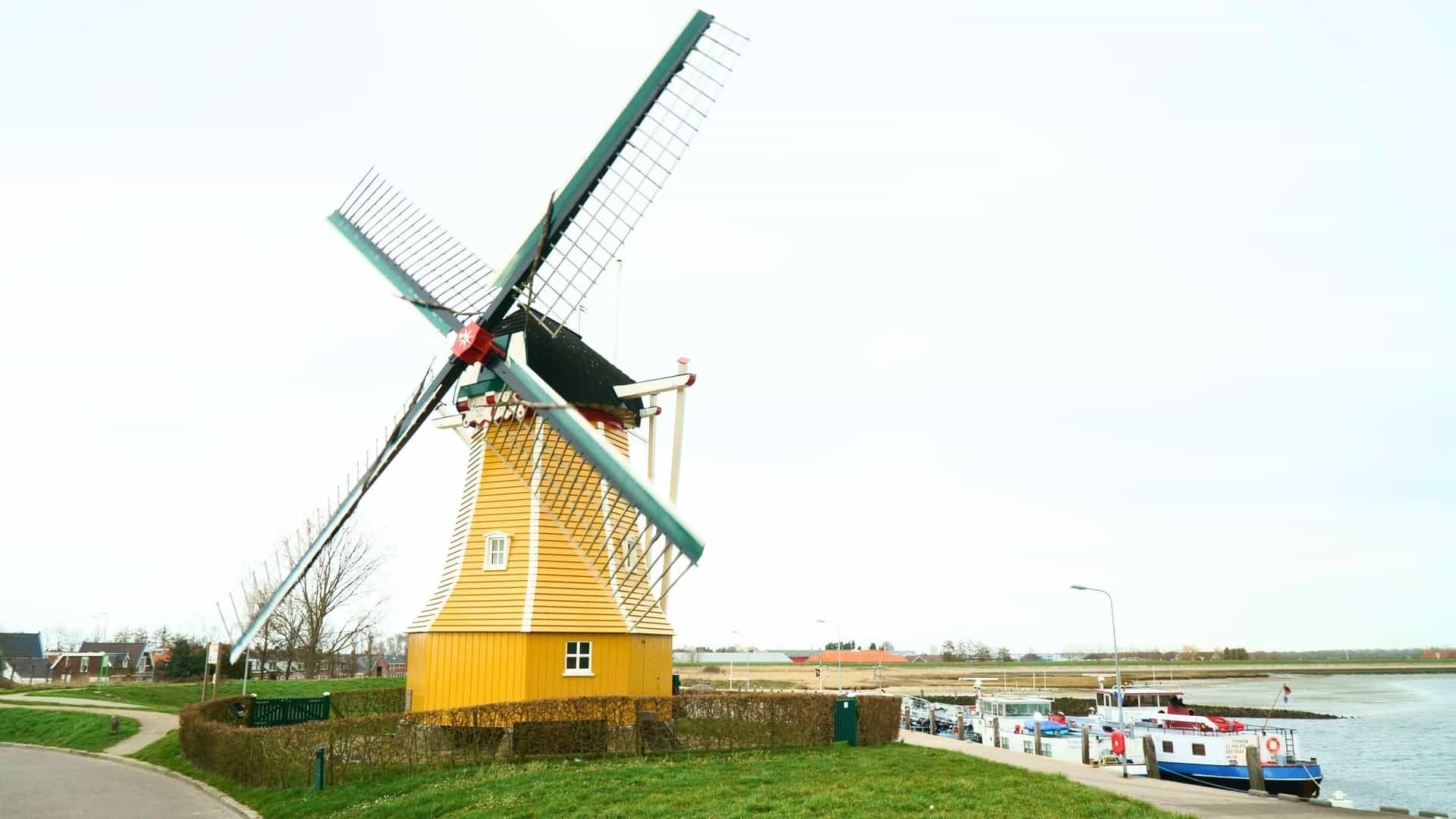A classic yellow windmill, a famous landmark of Bruinisse, Netherlands, stands next to a small harbor with boats.