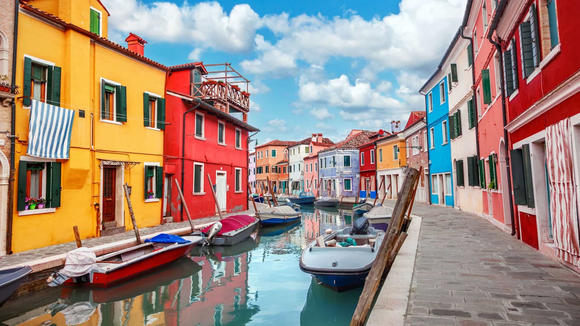 A picturesque canal on the Venetian island of Burano, Italy, lined with rows of vibrant, colorfully painted houses.