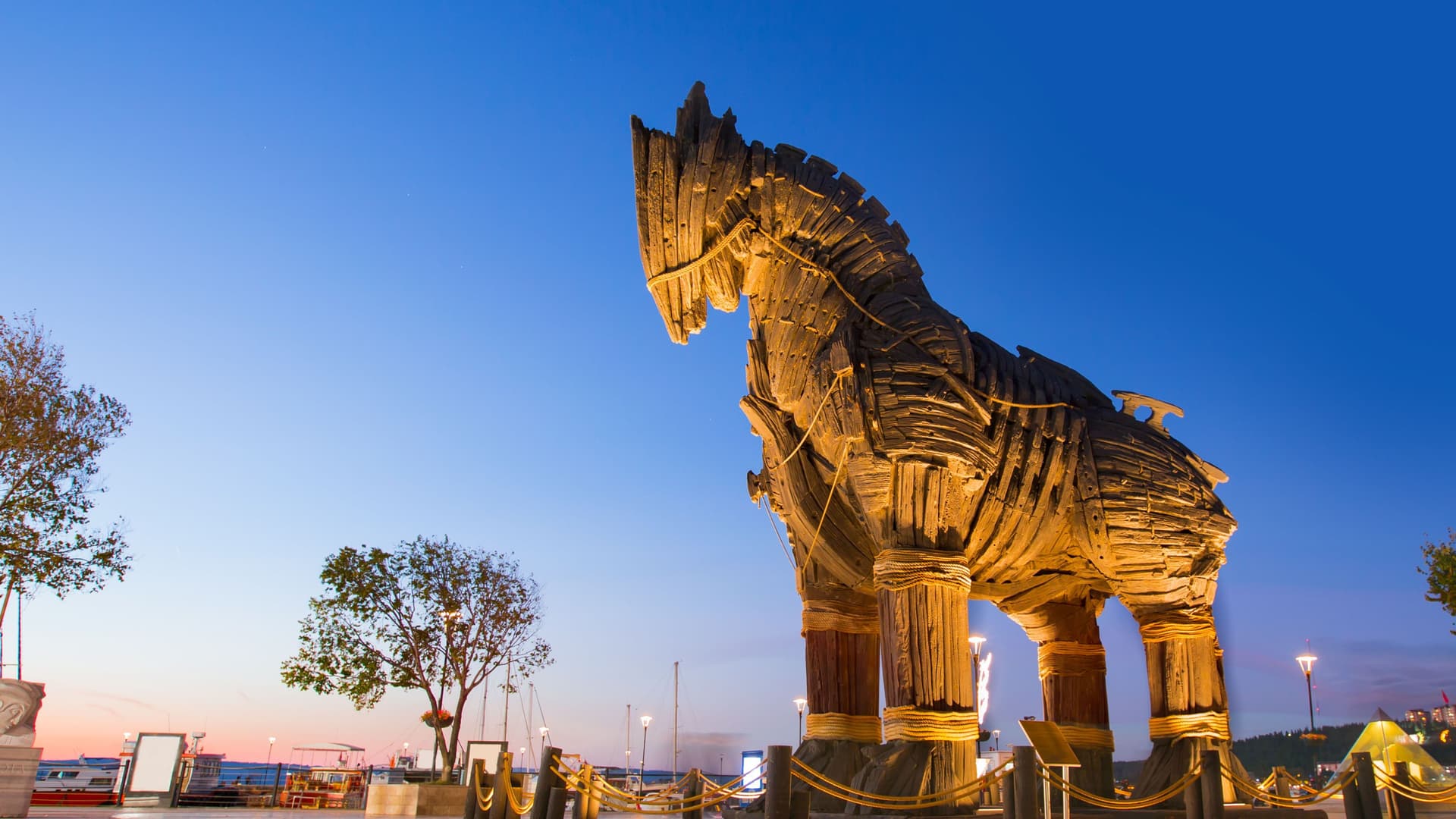 A stunning twilight image of the iconic wooden Trojan Horse statue, a famous landmark in Çanakkale, Turkey, against a deep blue and orange sky at sunset.
