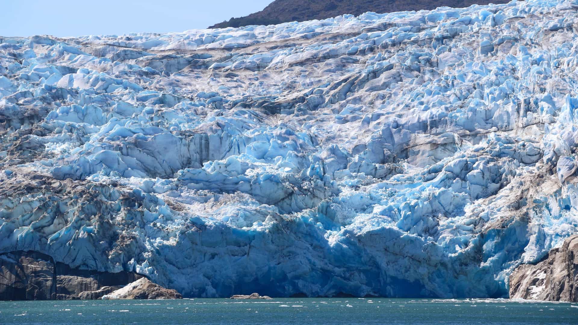 A massive, stunning blue and white glacier in the Sarmiento Channel, Patagonia, Chile, with its dramatic crevasses and ice formations towering over the deep blue water.