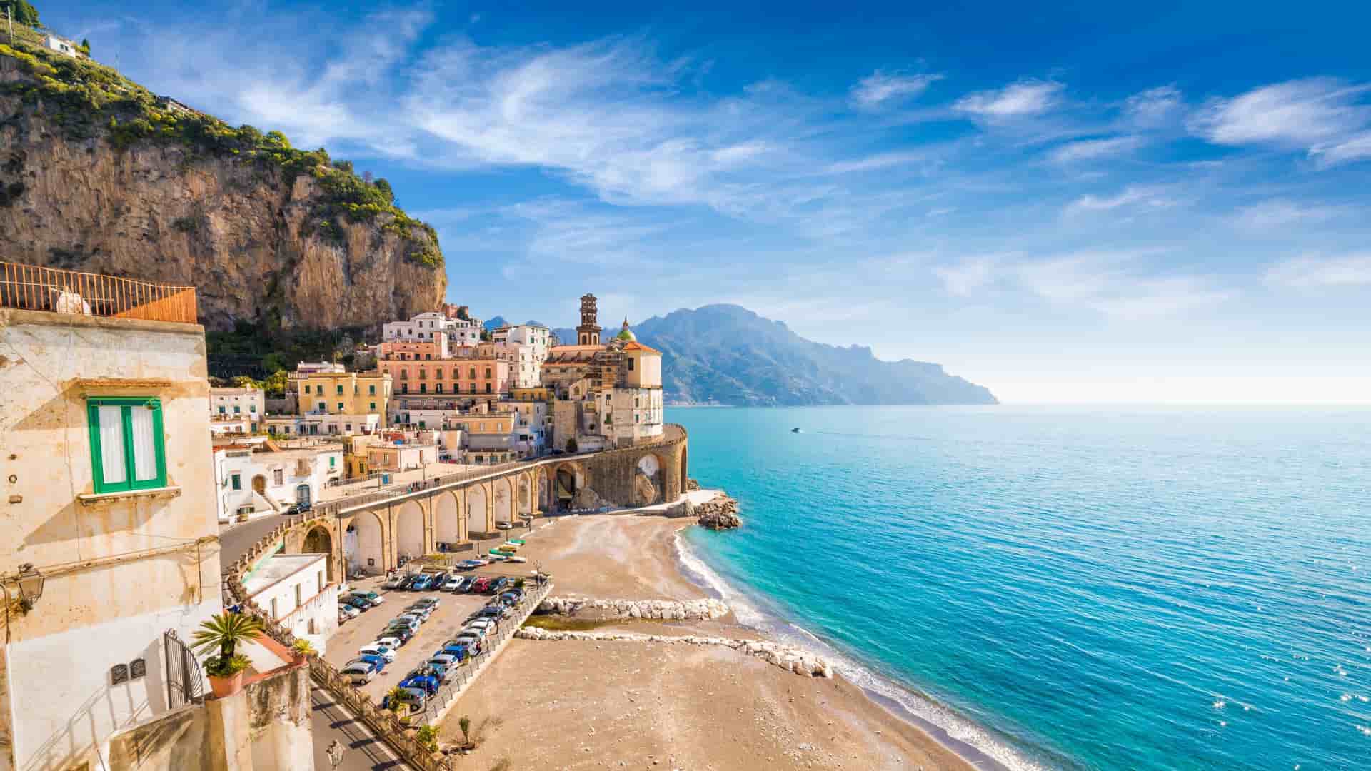 A scenic view of Capri, Italy, featuring a cliffside town with colorful buildings, a small beach, and the sparkling turquoise waters of the Mediterranean Sea.
