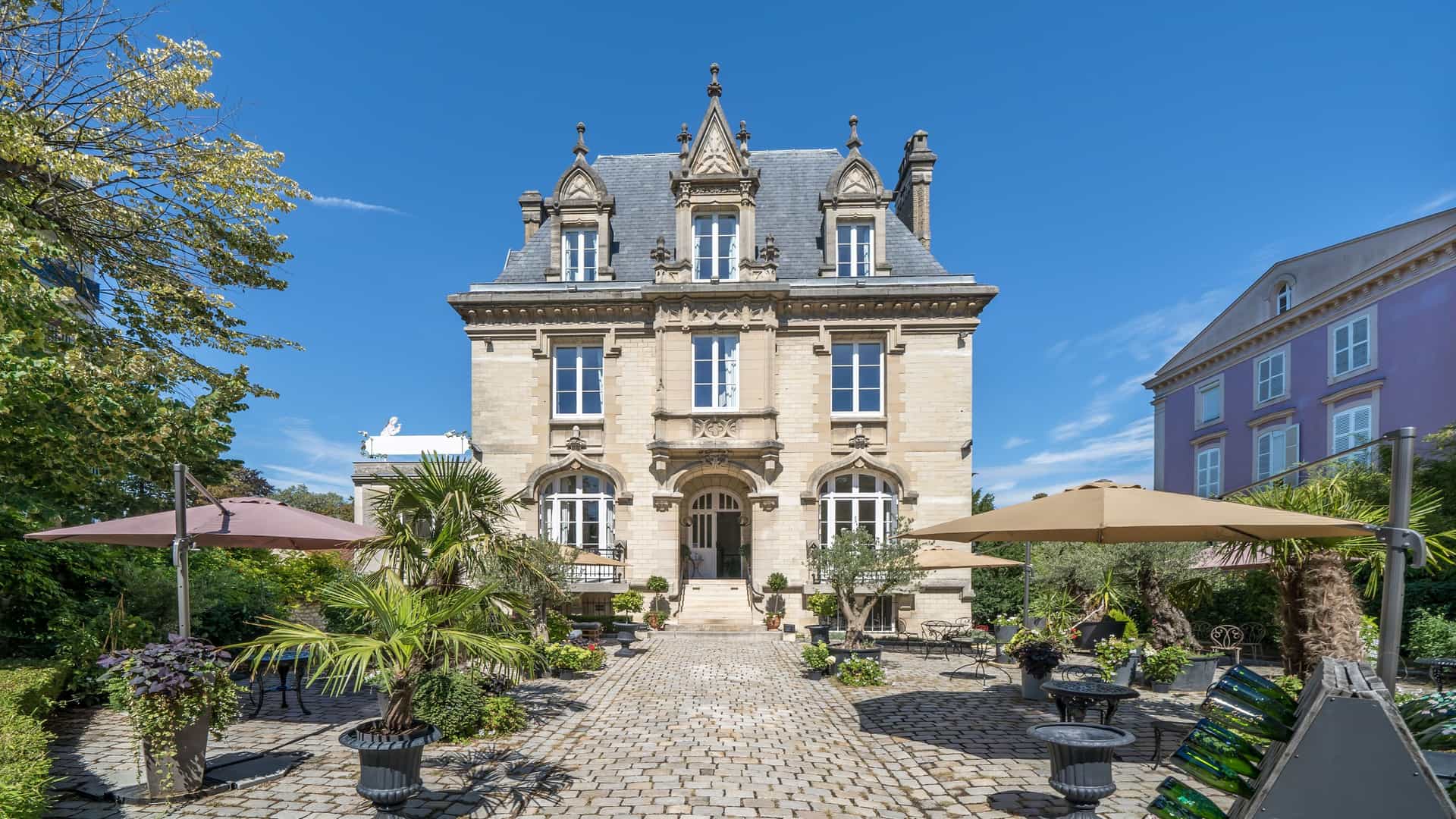 A grand, ornate stone chateau in the Champagne region of France, surrounded by a charming courtyard and lush gardens.