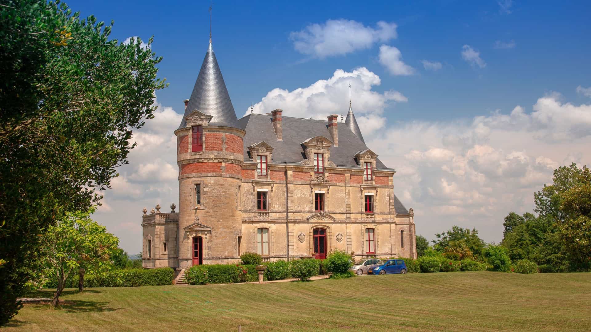 A stunning close-up of the Château de Rayne Vigneau, a grand Sauternes winery and estate in Bordeaux, featuring a beautiful castle with conical towers under a bright blue sky.