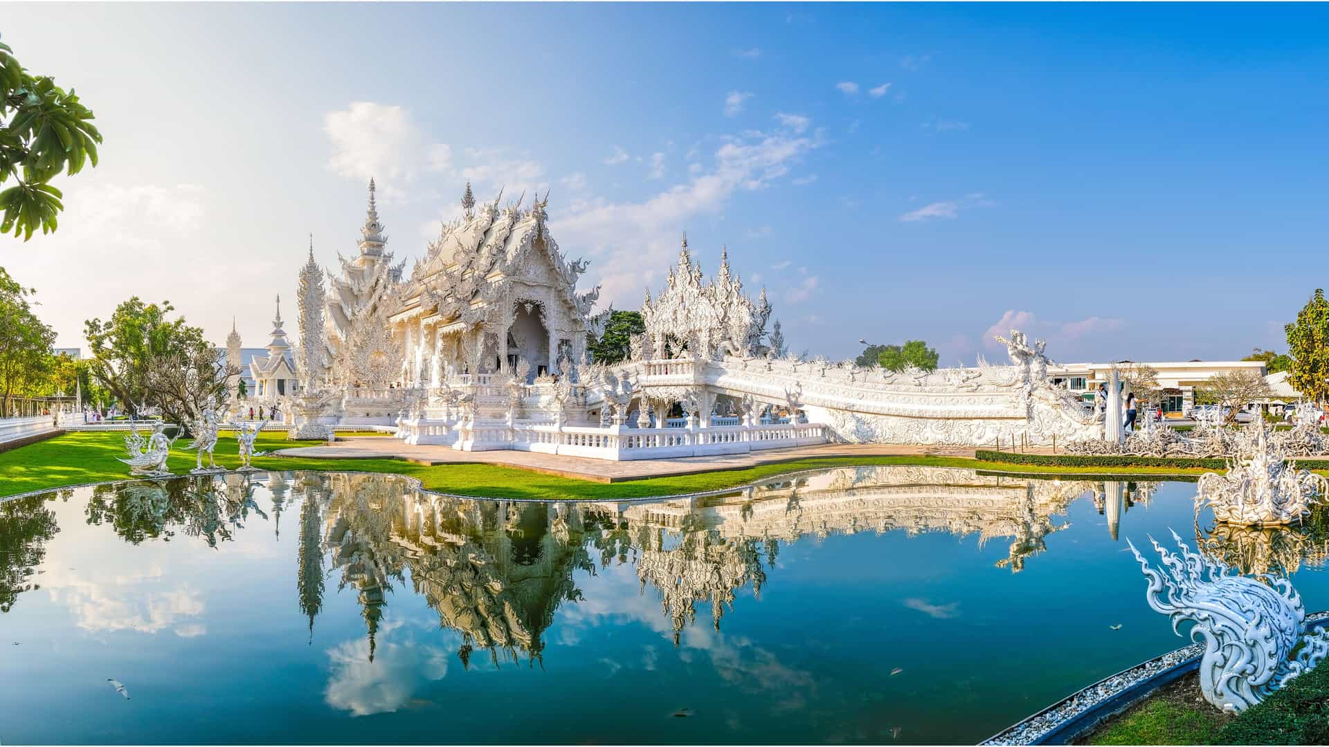 A breathtaking panoramic shot of the stunning white temple, Wat Rong Khun, in Chiang Rai, Thailand, with its ornate and intricate architecture perfectly reflected in the serene lake.