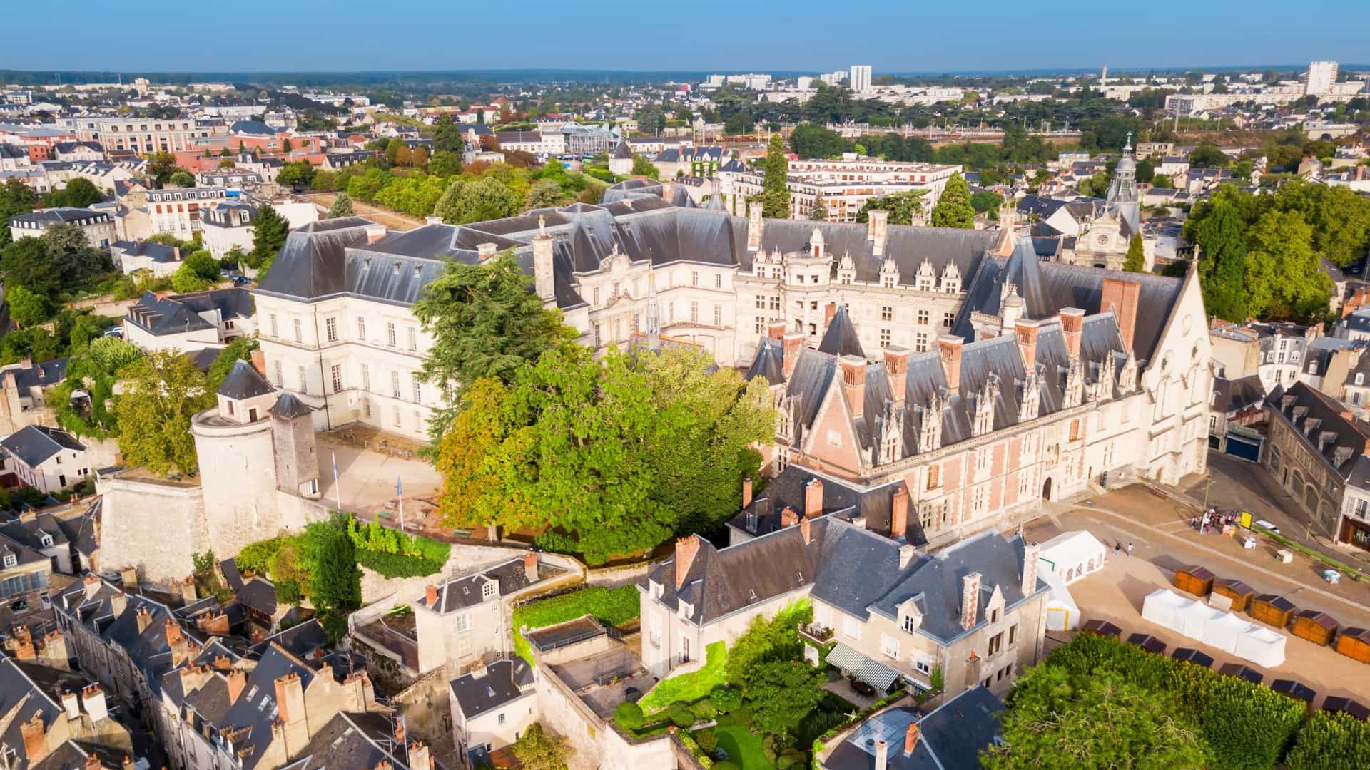 An aerial view of the historic Chateau de Blois in France, featuring its Renaissance architecture and towers surrounded by a cityscape with a clear blue sky.