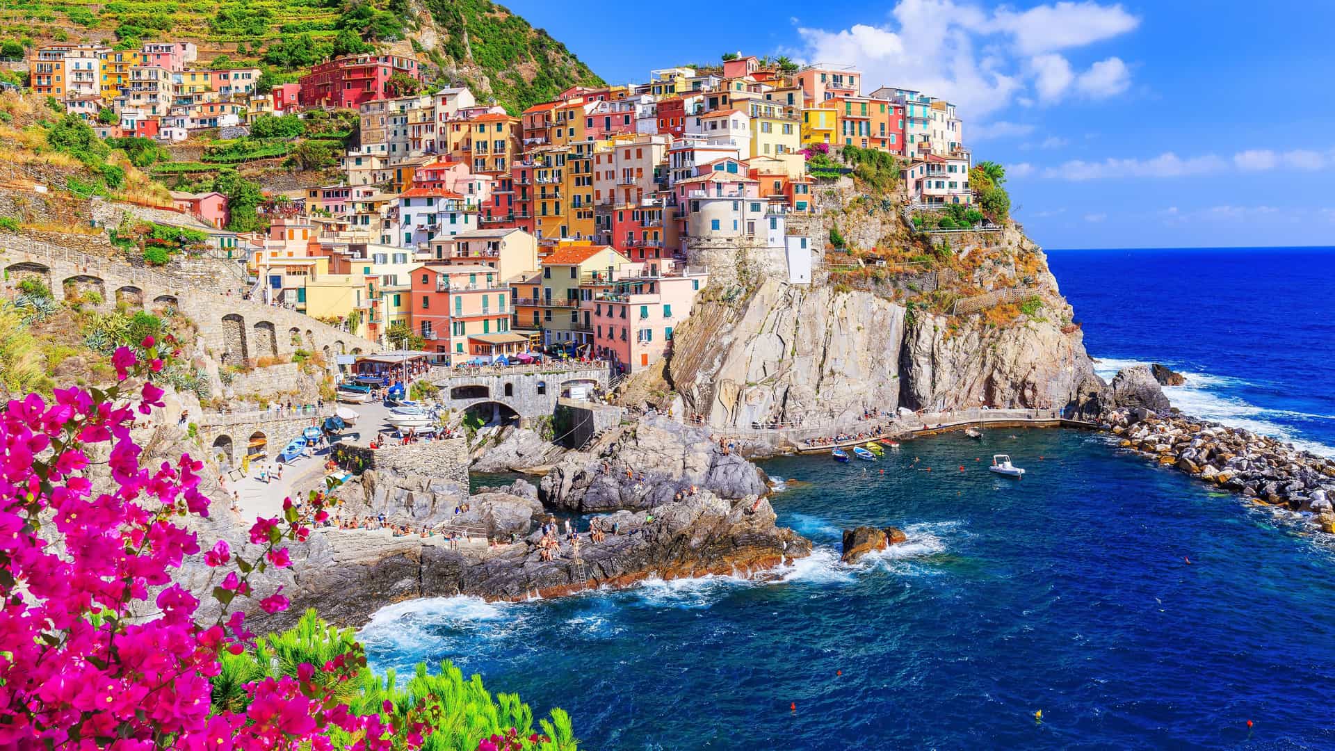 A colorful and picturesque shot of the village of Manarola in Cinque Terre, Italy, with its vibrant pastel-colored houses clinging to the cliffside overlooking the deep blue Ligurian Sea.