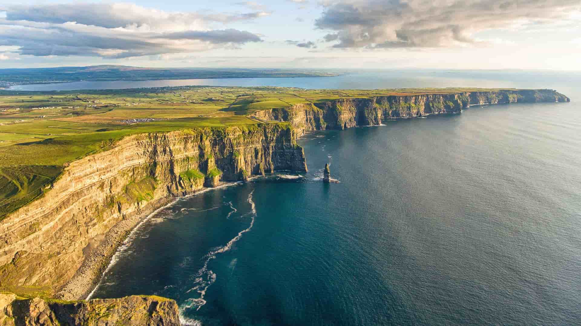 An aerial view of the iconic Cliffs of Moher in Ireland, showcasing the dramatic sea cliffs plunging into the Atlantic Ocean under a beautiful sunset sky.