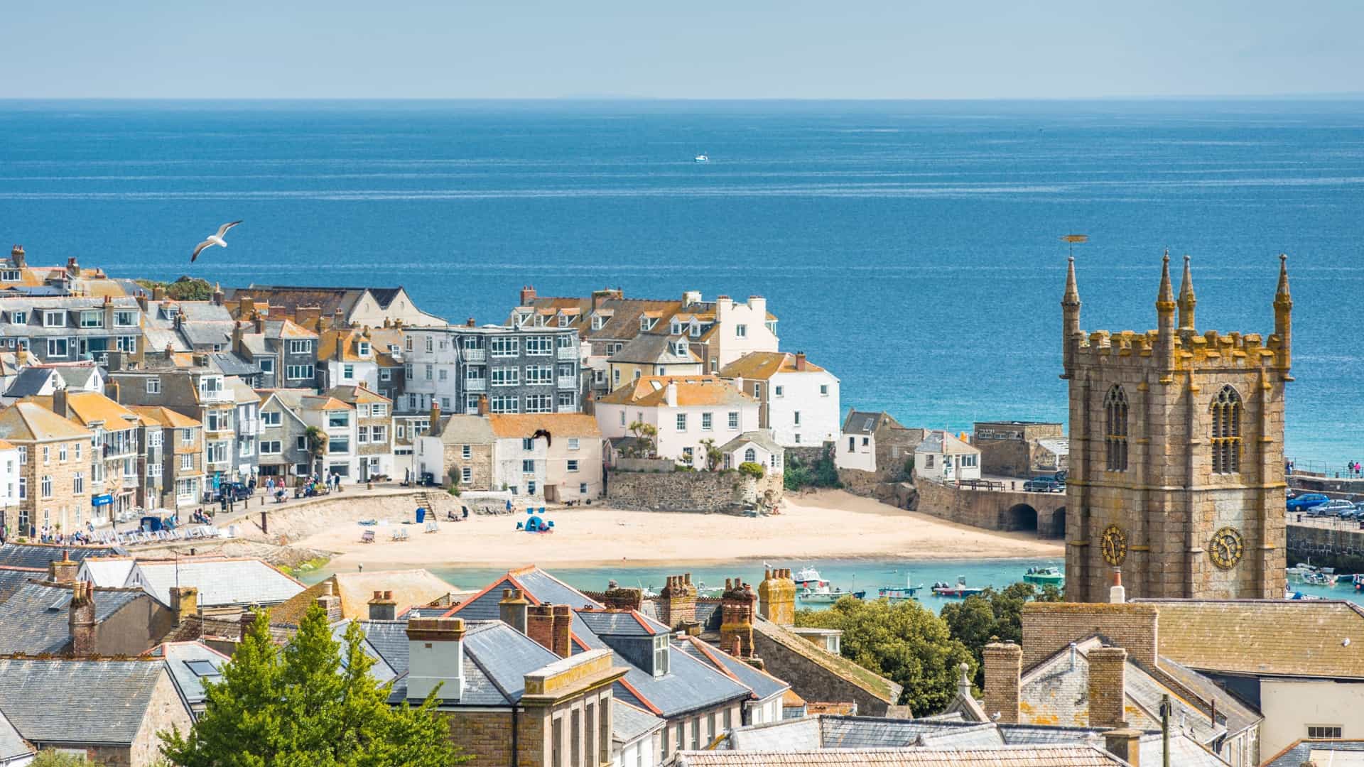 Scenic view of St. Ives coastal town in Cornwall, UK. St. Ia's Church tower overlooks the harbor beach and the blue Atlantic Ocean.