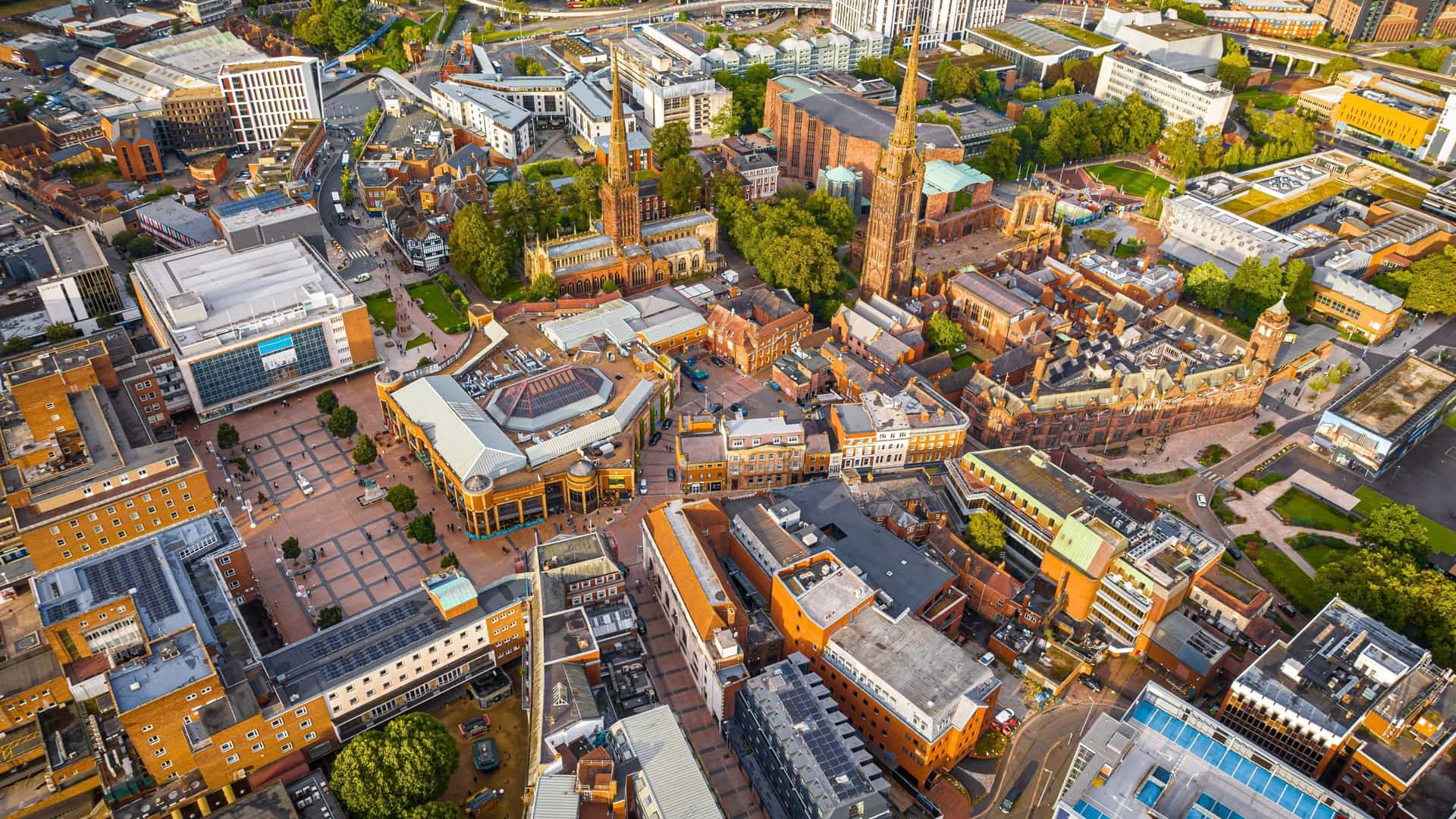 An aerial view of Coventry, a city in Central England. The photo highlights the dense urban landscape, featuring a mix of modern and post-war architecture. The image is notable for featuring key landmarks like the ruins of the medieval Coventry Cathedral (St Michael's) next to the modern, new Coventry Cathedral. The city is known for its history, including its devastation during World War II, and its association with the statue of Lady Godiva.